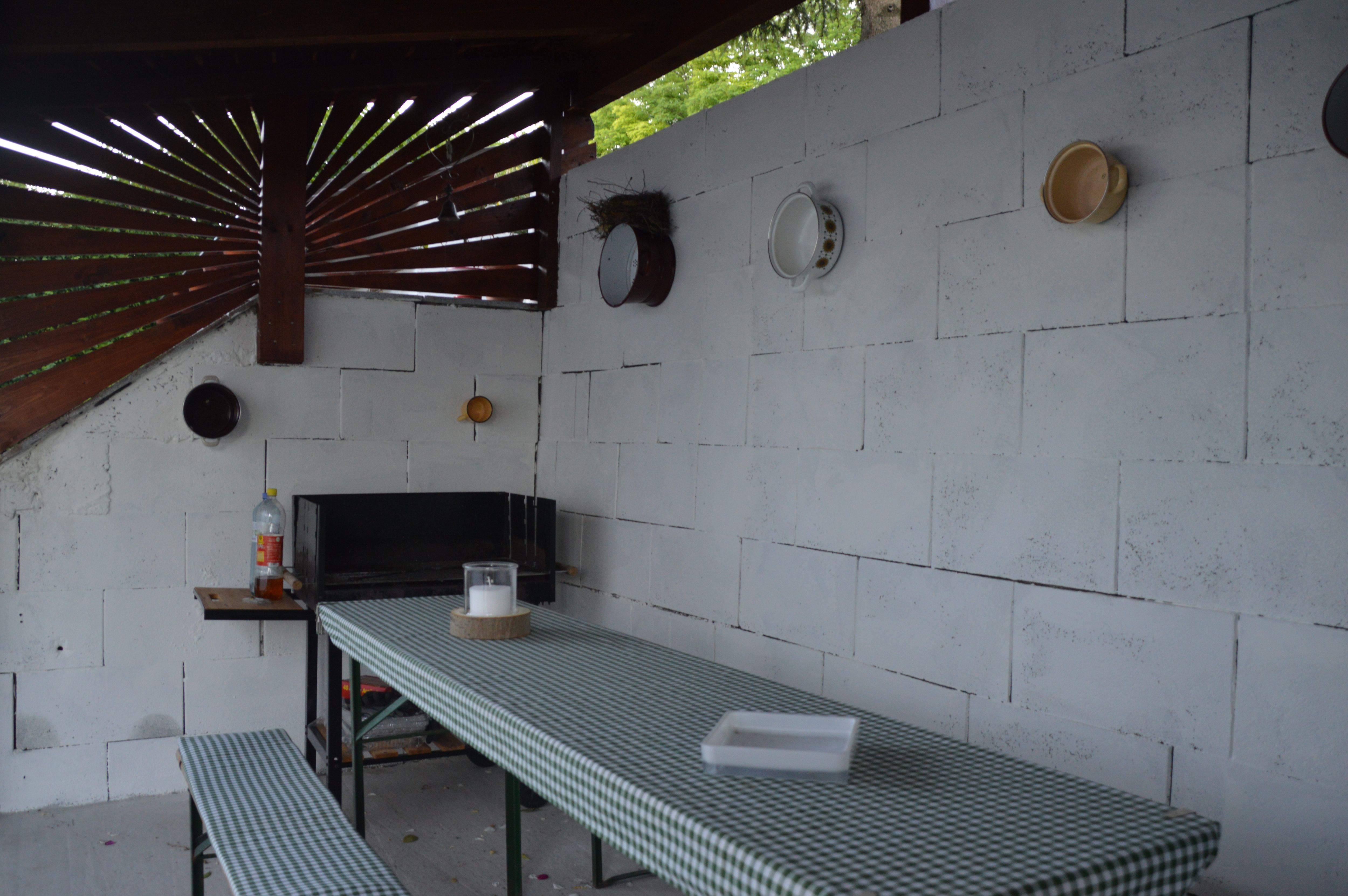 Covered barbecue area with table and benches, decorated with crockery on the wall.