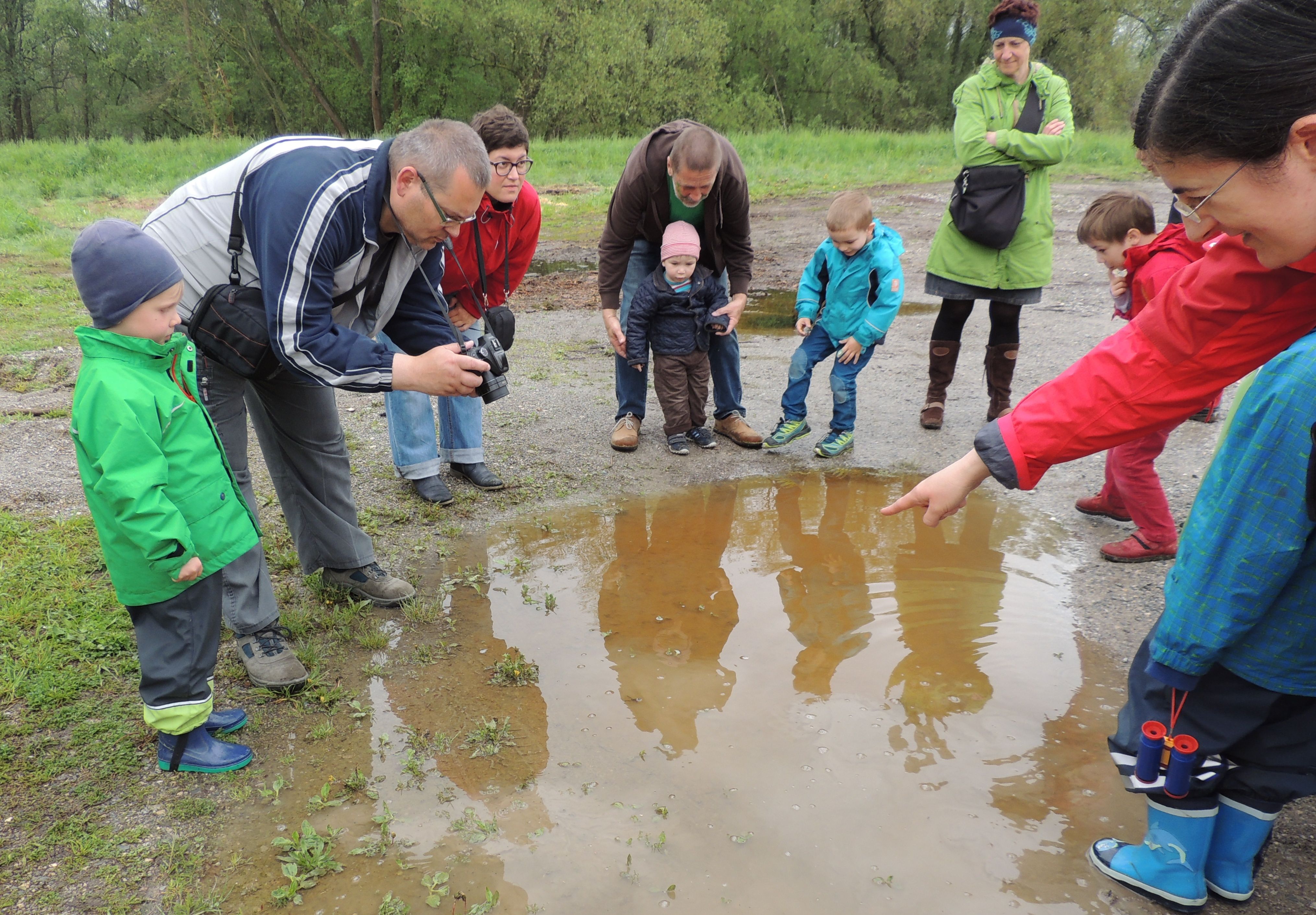 Group of adults and children watching a puddle outdoors.