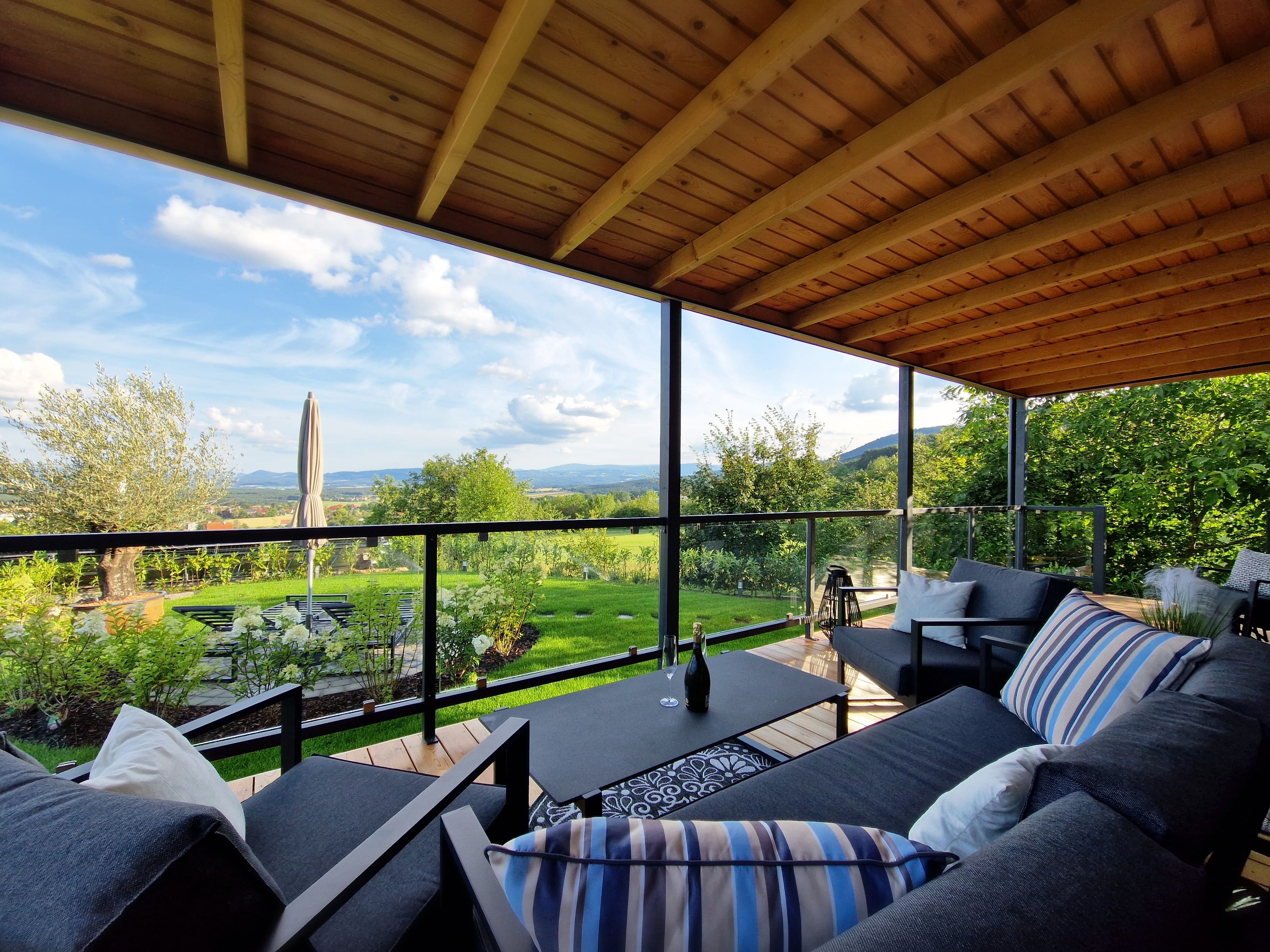 Covered terrace with modern furniture and views of the green landscape.
