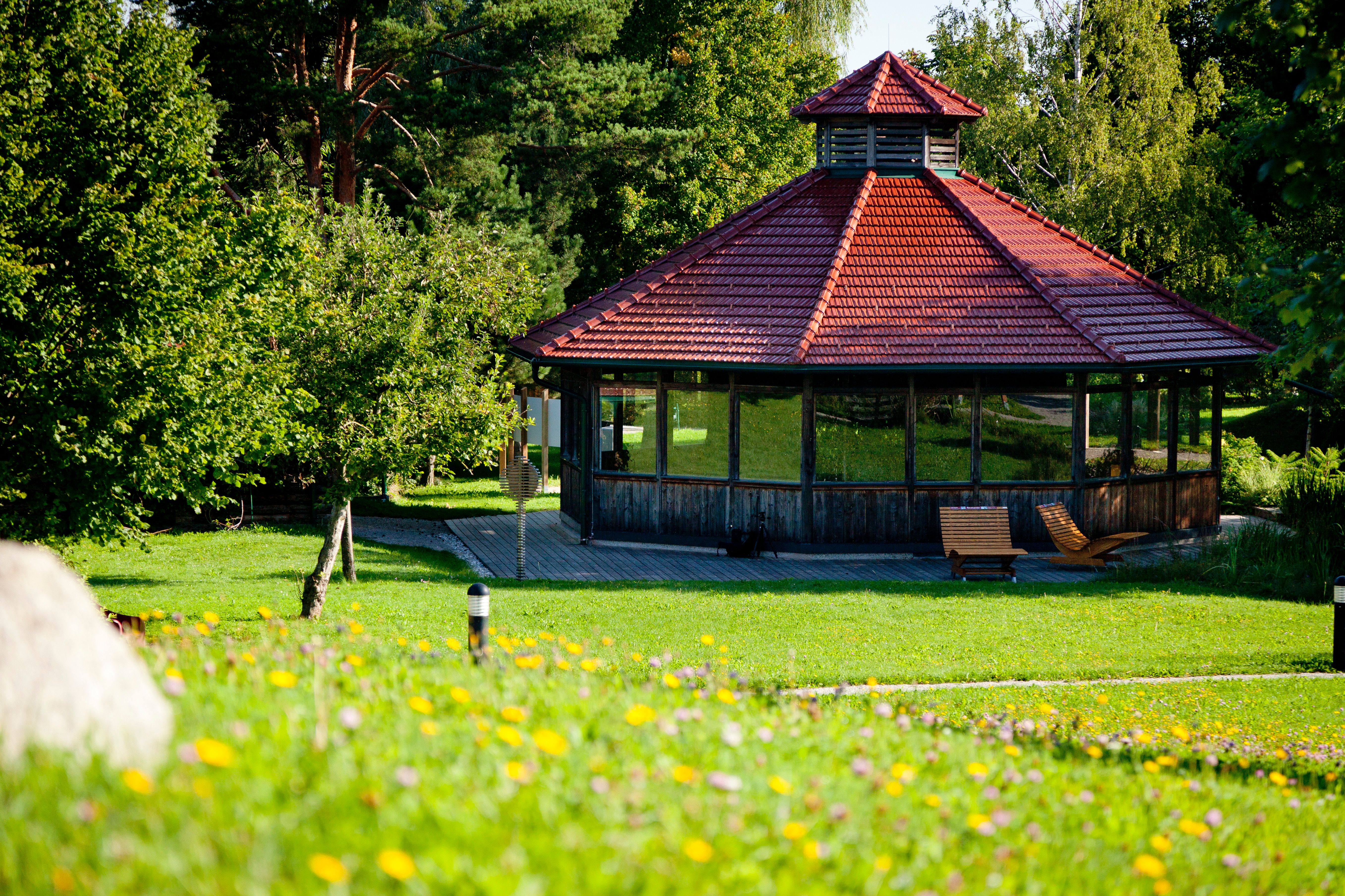 A pavilion with a red roof in a green park, surrounded by trees and flowers.