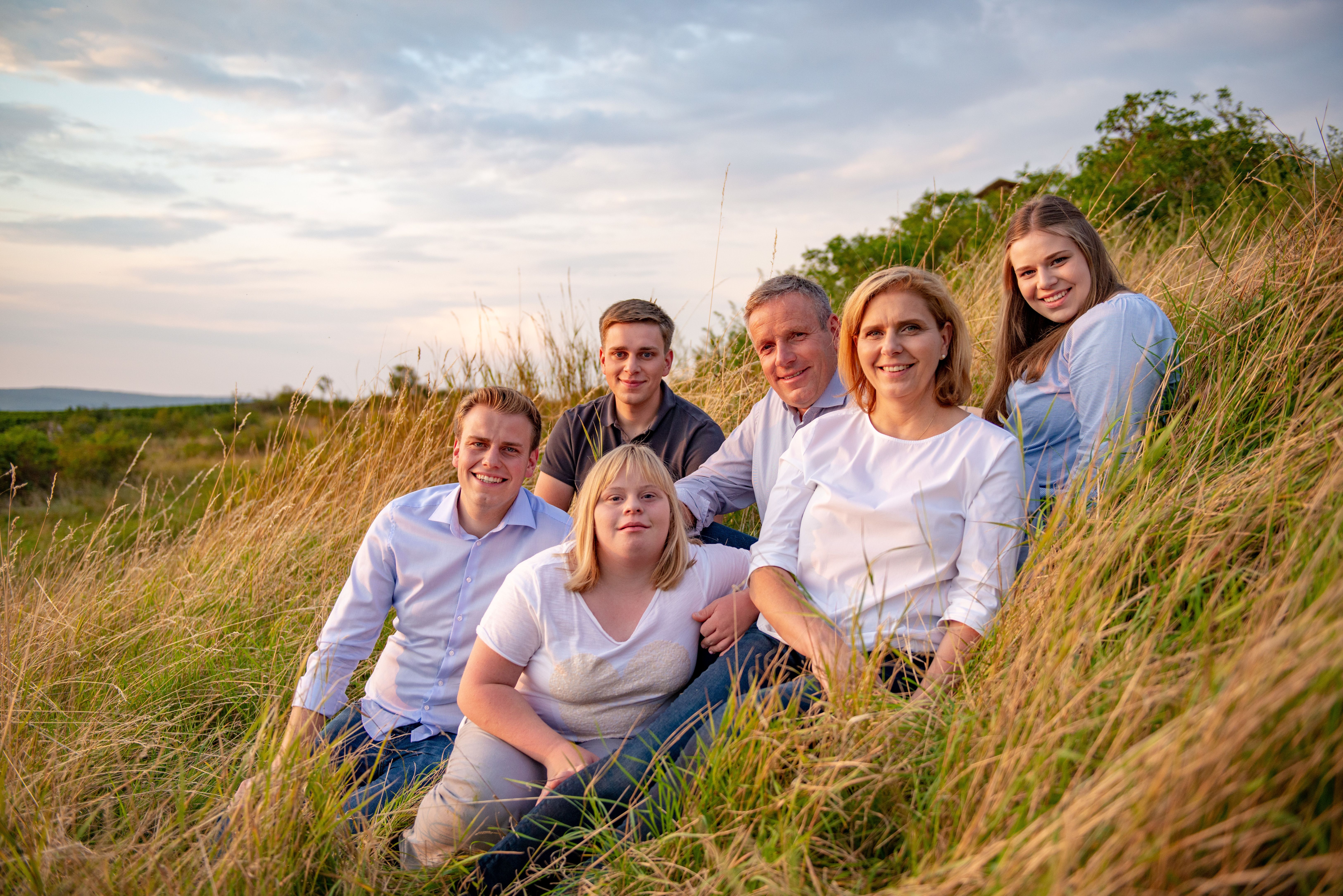 A group of six people sit in a field at sunset.