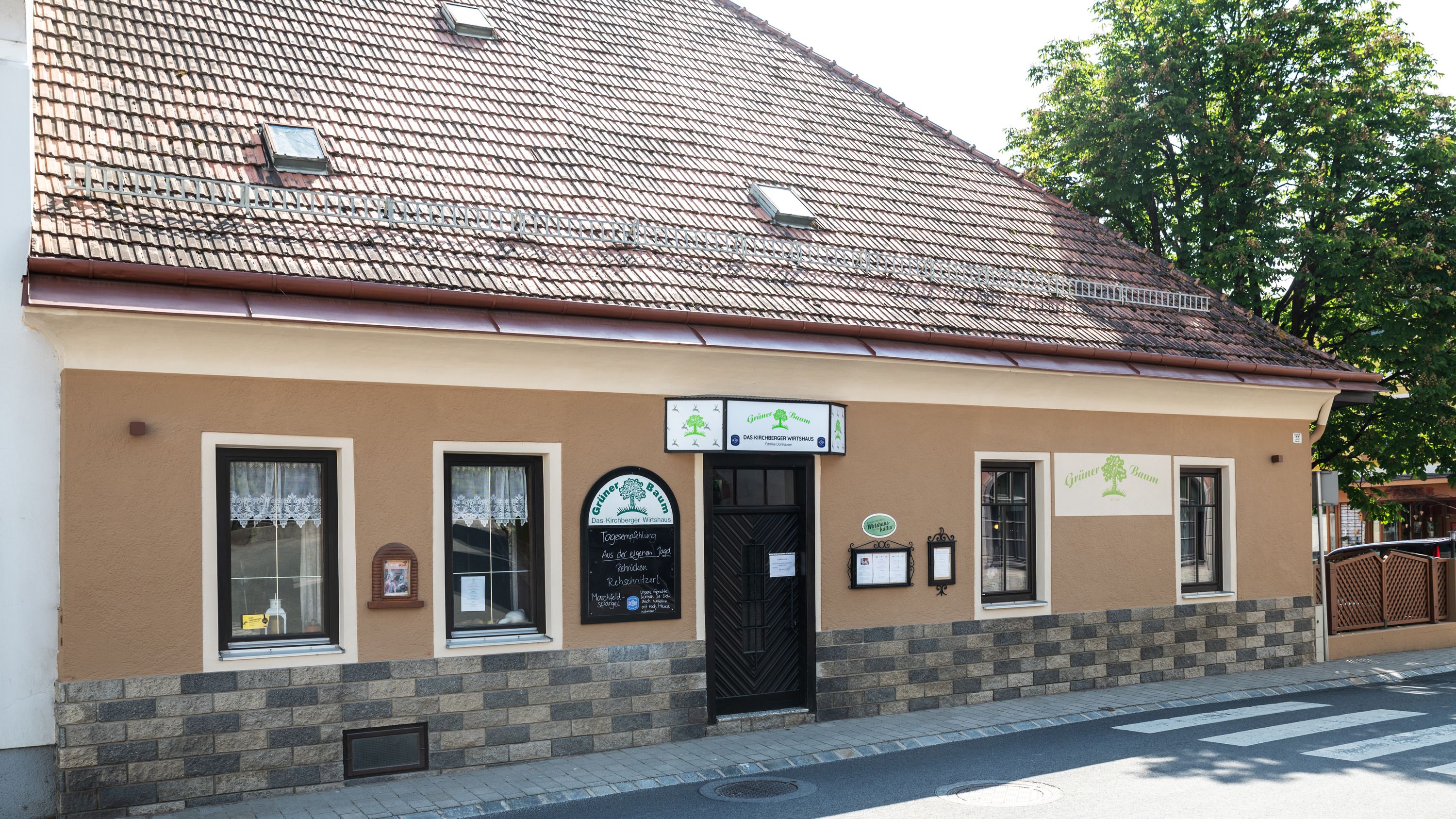 Historic building with brown façade and signs. It has a tiled roof and windows with curtains.