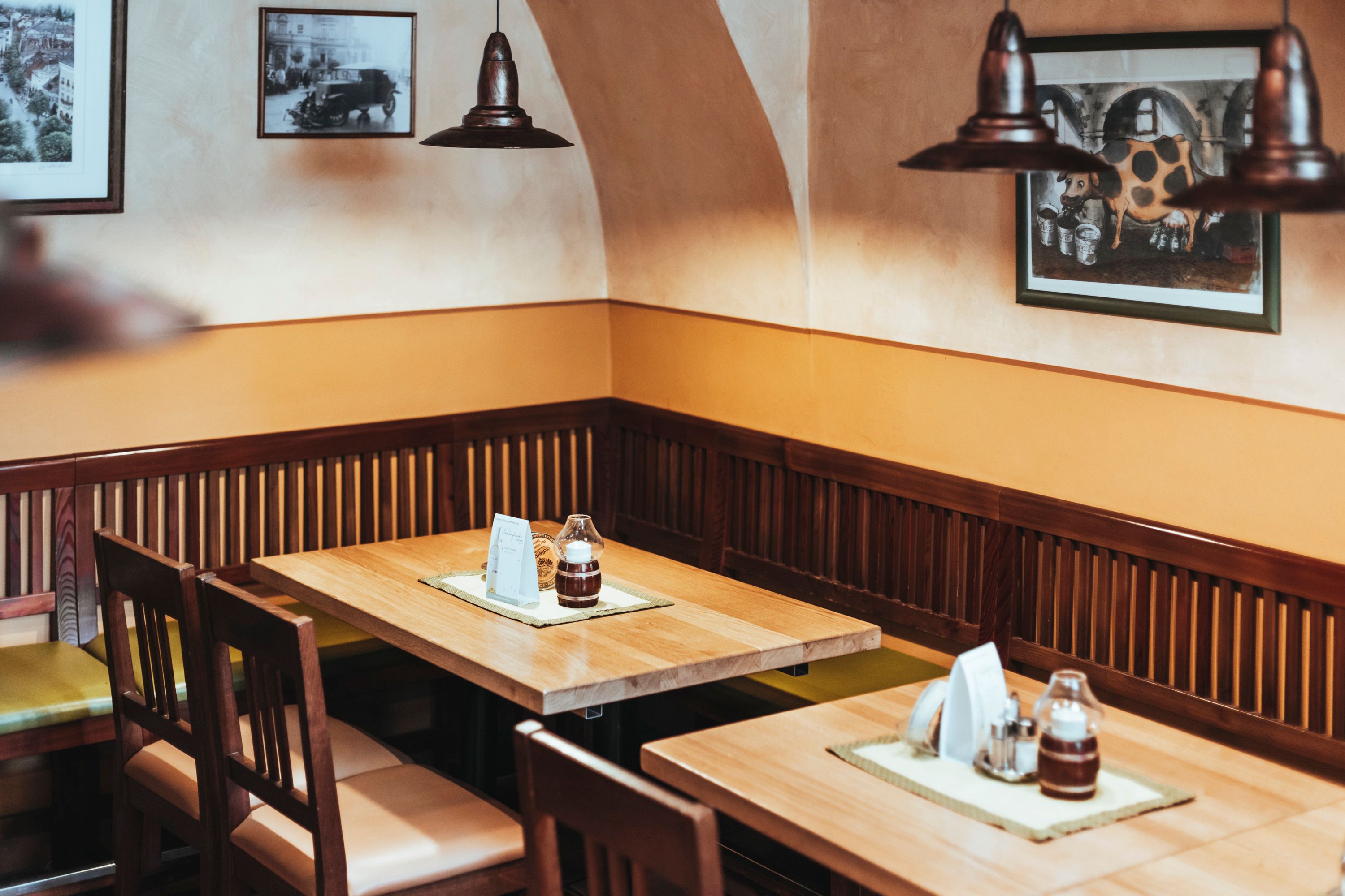 Cozy seating area in a restaurant with wooden tables and chairs, decorated with pictures on the wall.