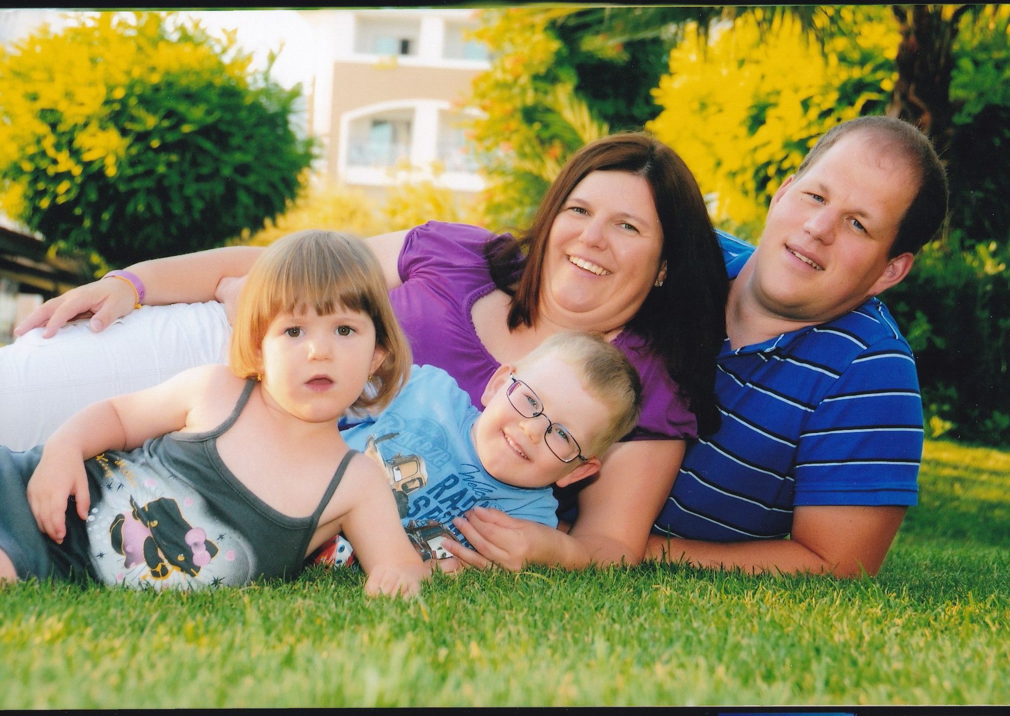 A family lies smiling on a meadow, consisting of two adults and two children.
