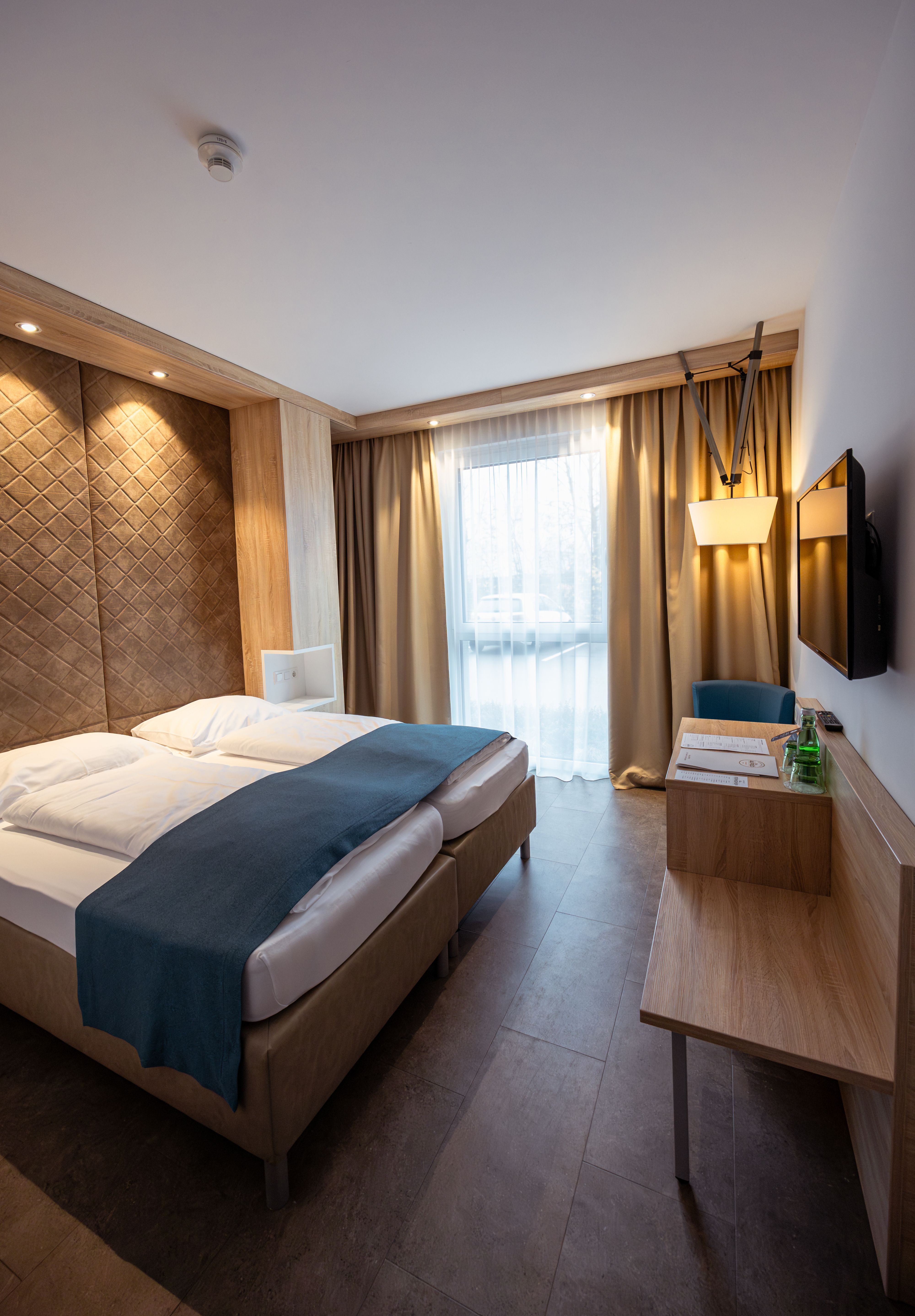 Modern hotel room with double bed, wooden paneling and windows with curtains.