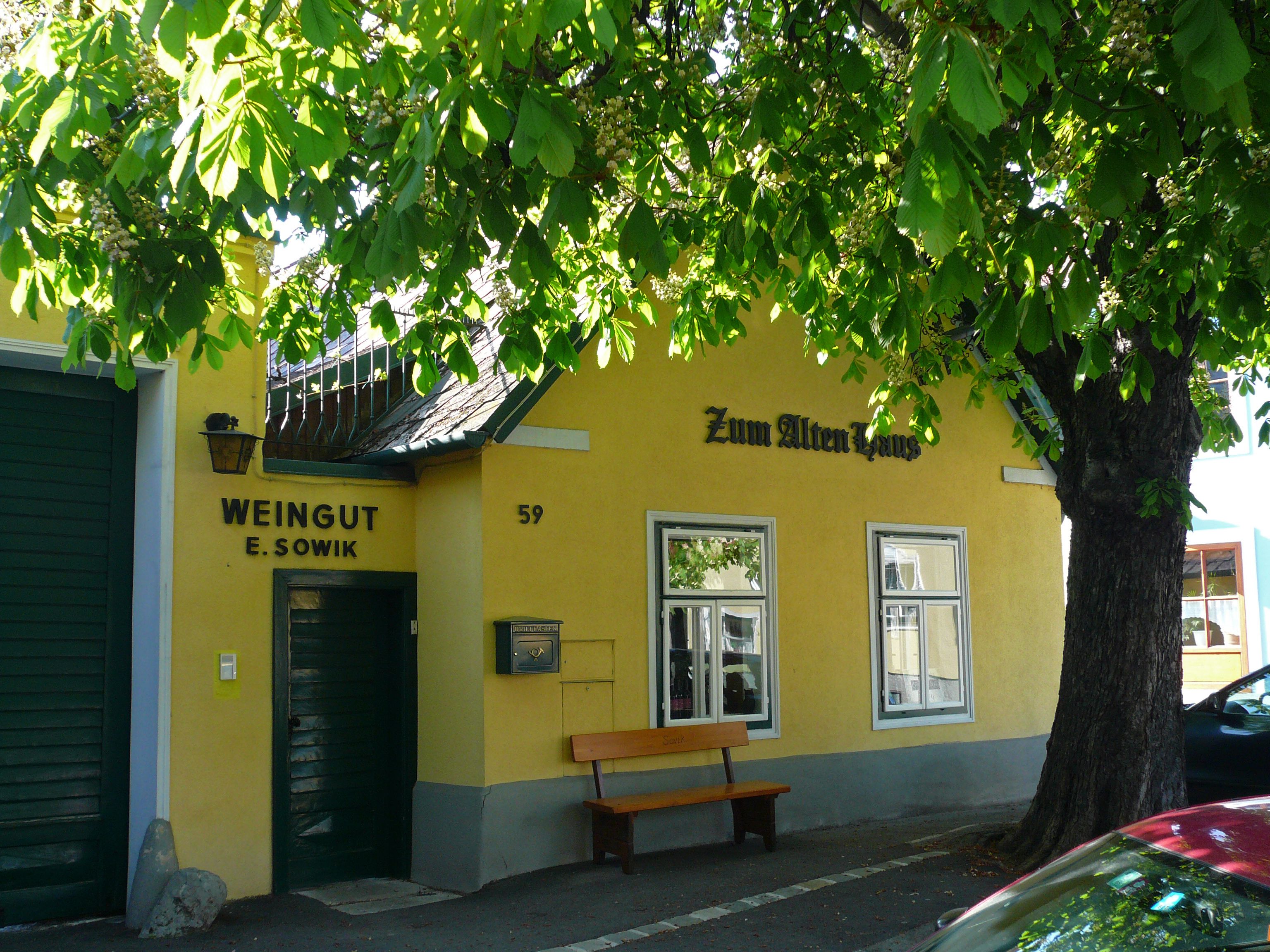 Yellow building with the inscription 'Zum Alten Haus' and 'Weingut E. Sowik', surrounded by green trees.