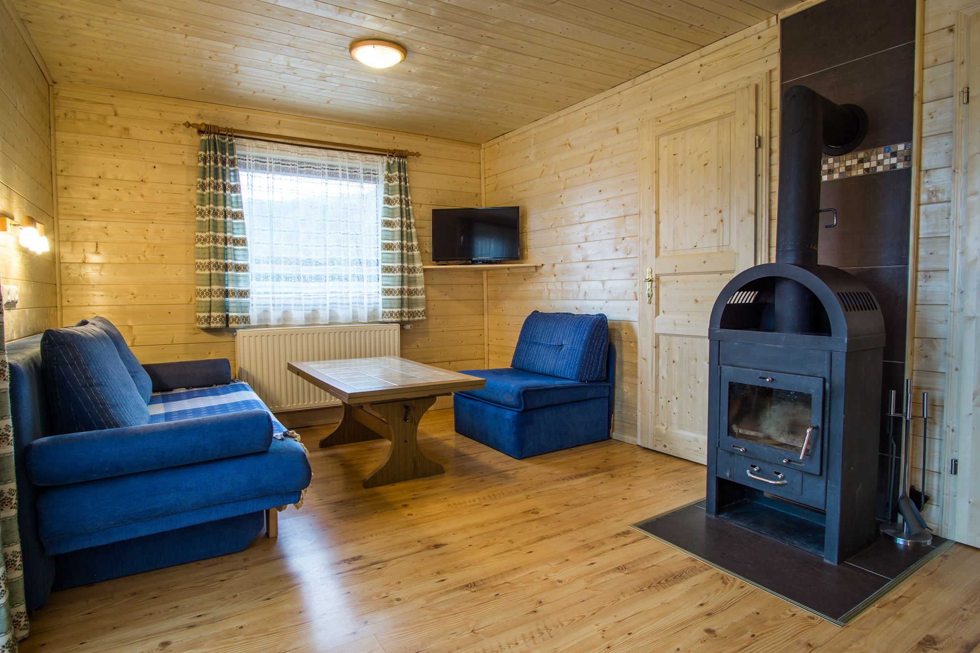 Cozy living room with wooden walls, blue sofas, wooden table and wood-burning stove.