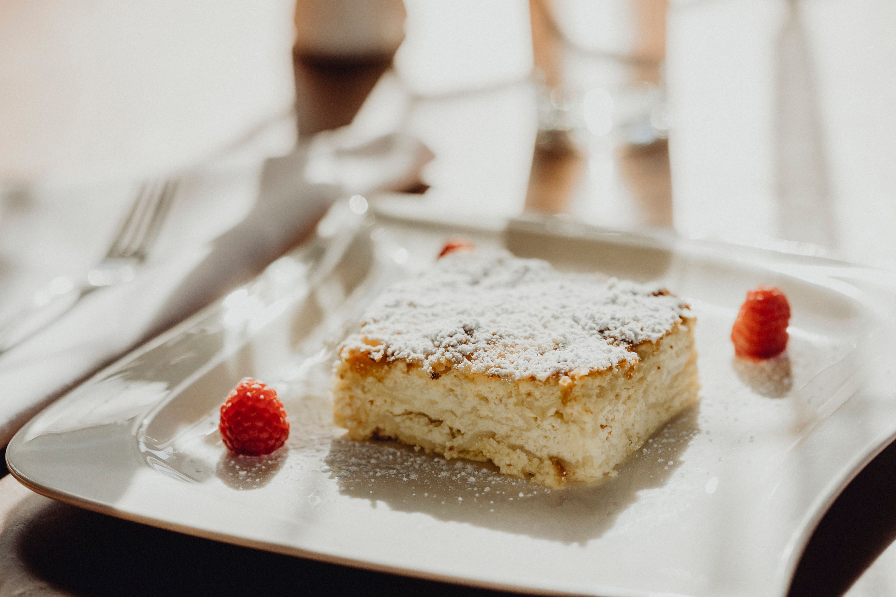 A slice of milk cream strudel with powdered sugar and raspberries on a white plate.