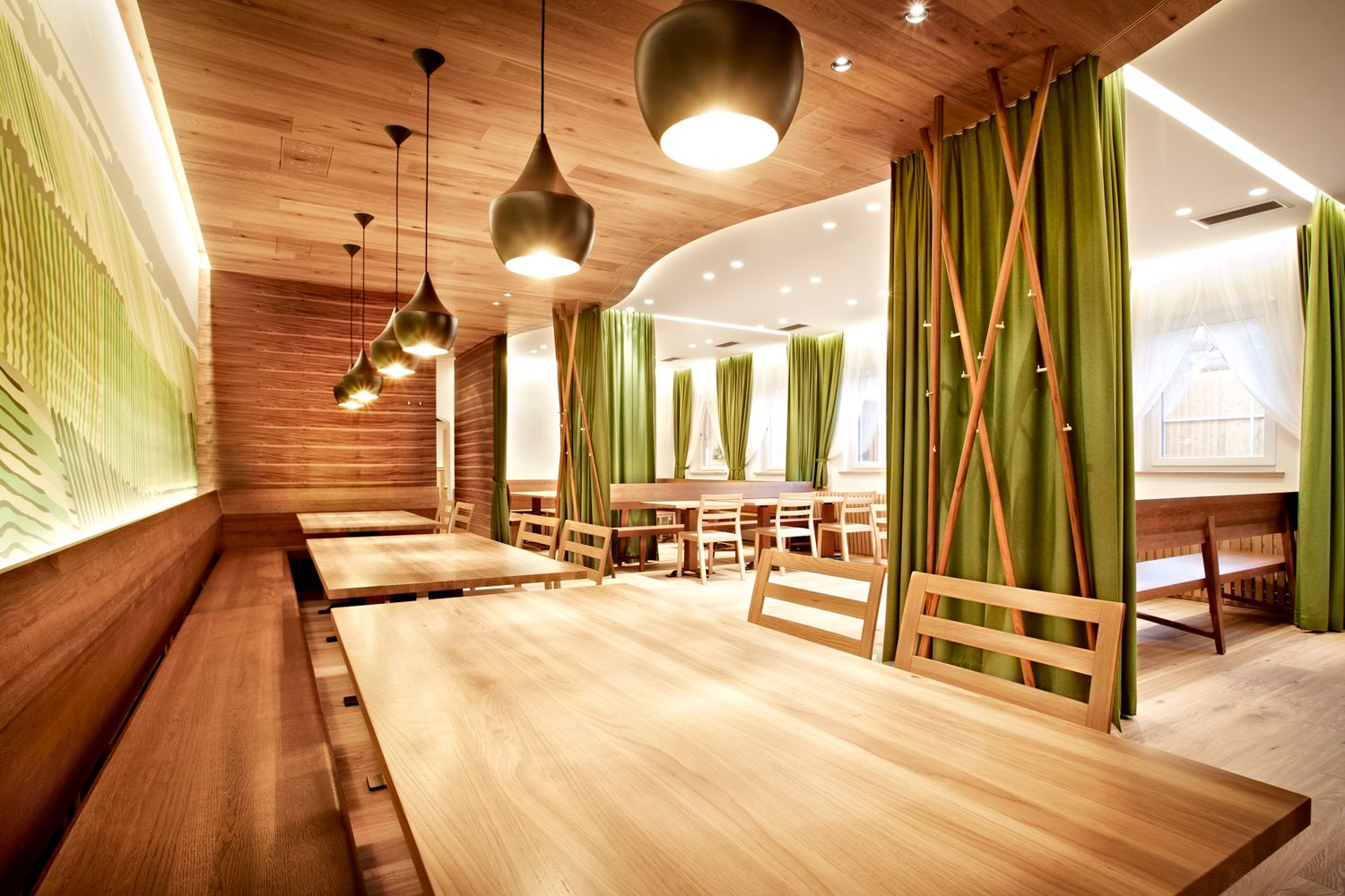 Modern restaurant with wooden tables and green curtains.