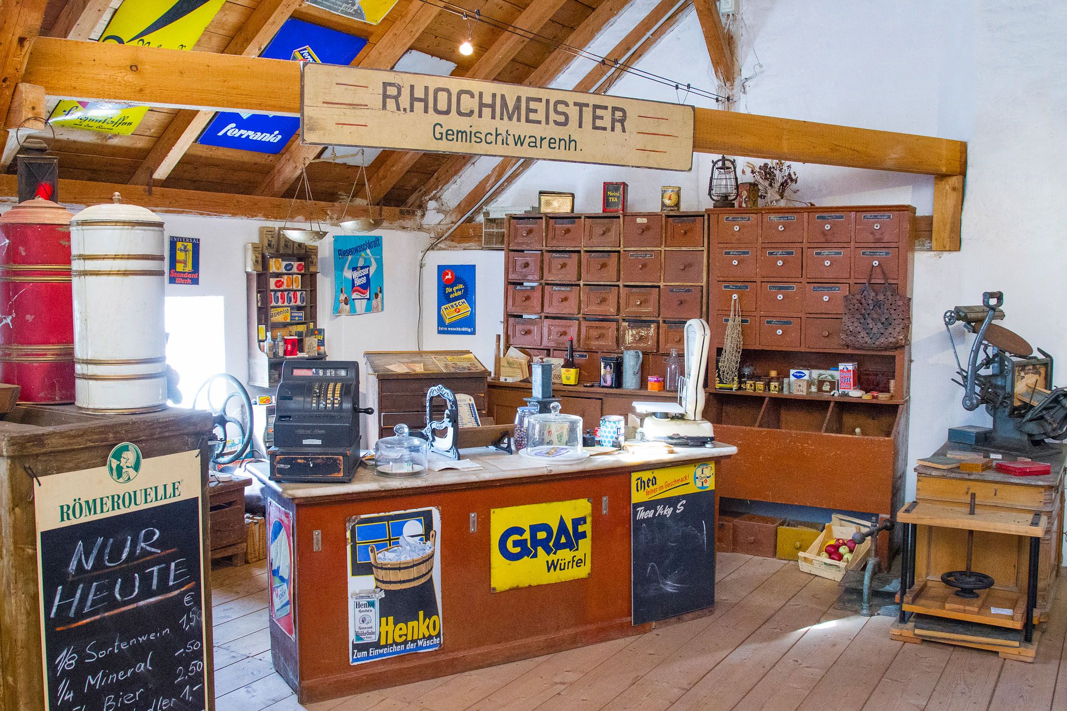 Interior view of an old general store with wooden furniture, a cash register and advertising signs on the walls.