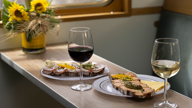 Two glasses of wine and sandwiches on a table with sunflowers in the background.
