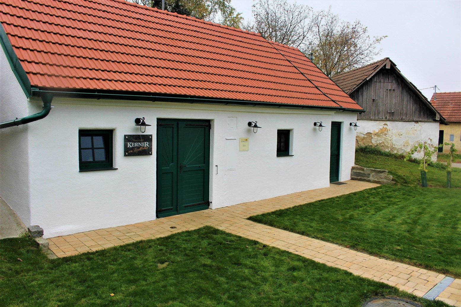 White building with a red roof and green doors, surrounded by lawn.