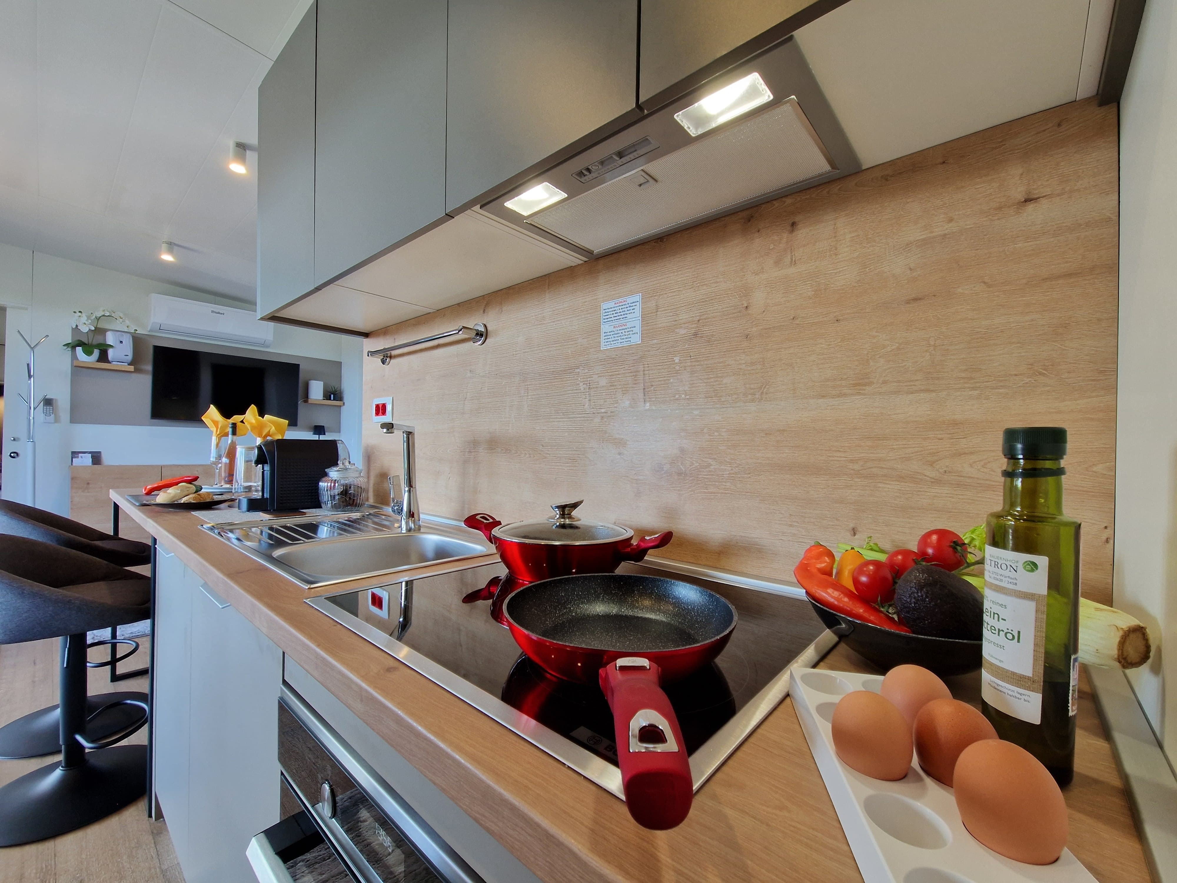 Modern kitchen with pans, vegetables, eggs and oil bottle on the worktop.