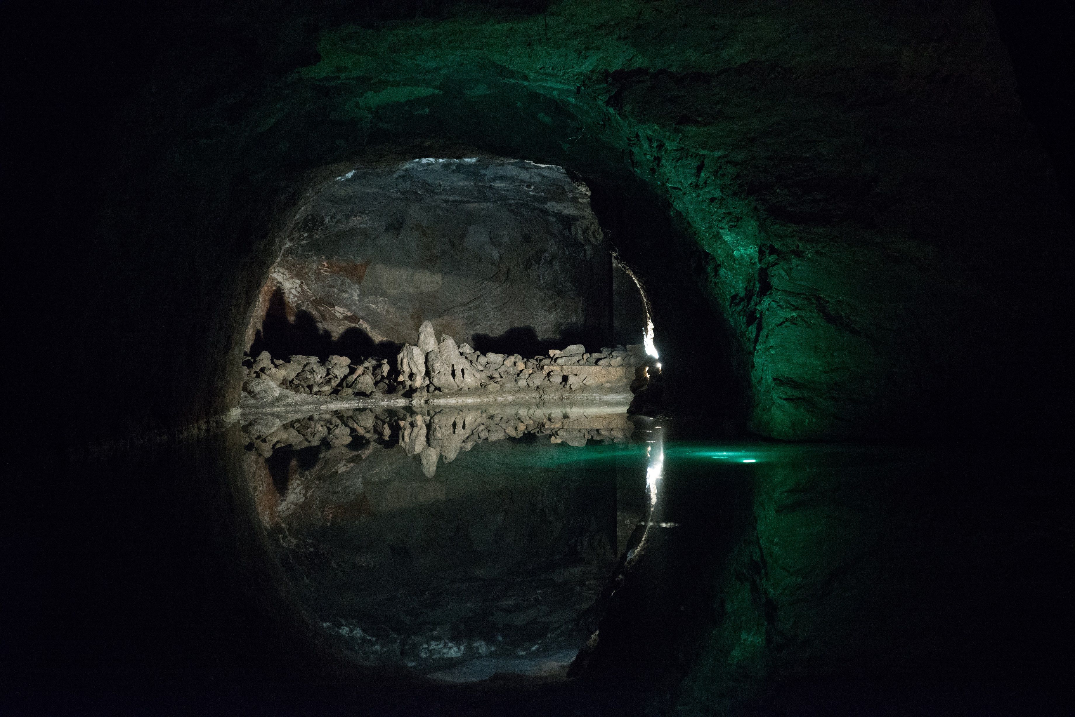 Dark cave with water and rock formations, illuminated by greenish light.