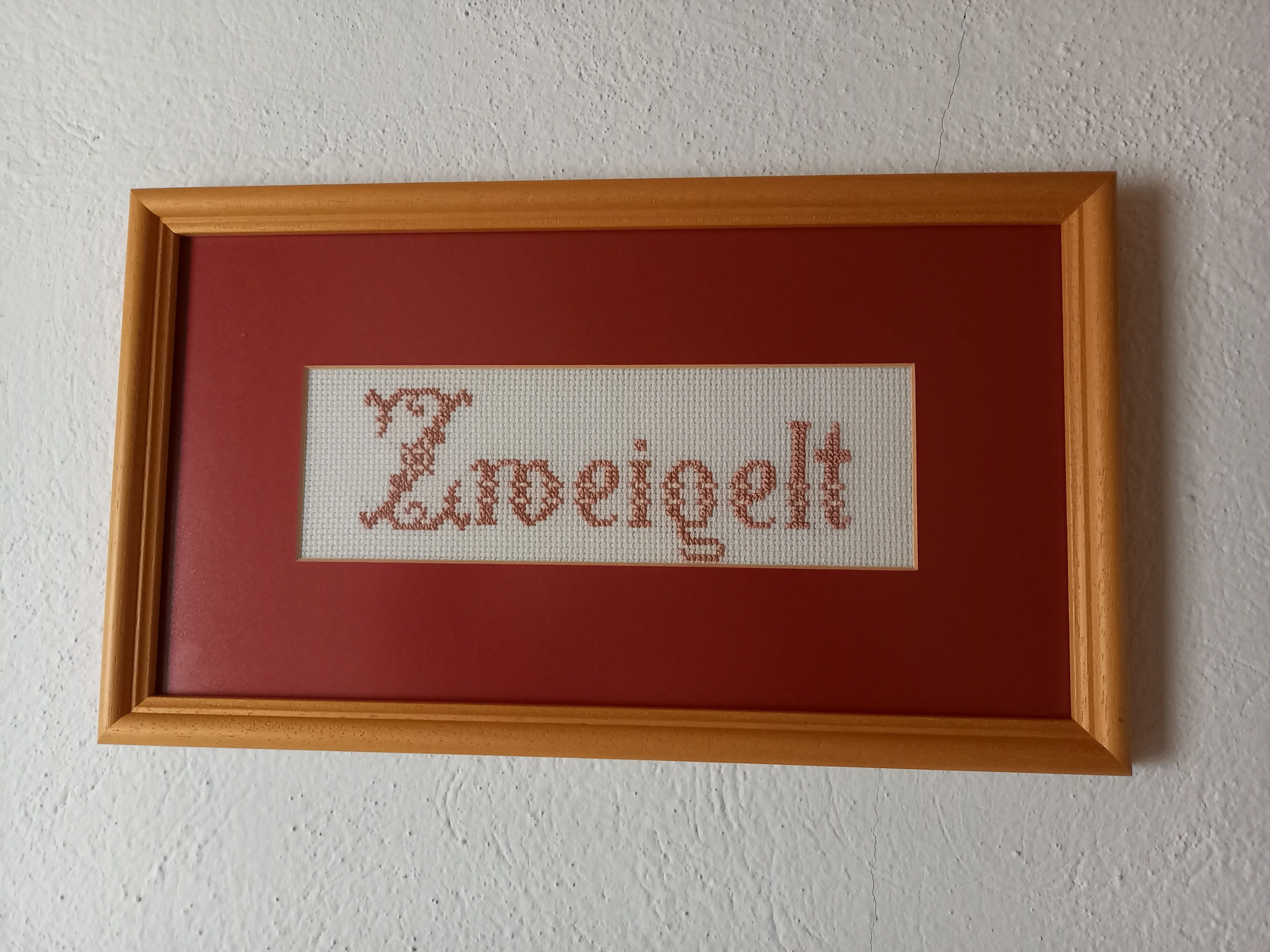 Embroidered picture with the word 'Zweigelt' in a wooden frame.