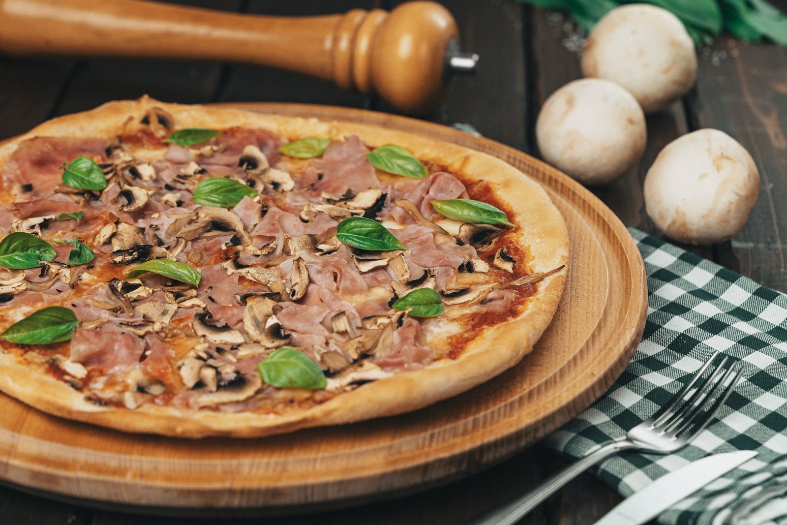 Pizza with ham, mushrooms and basil on a wooden board.