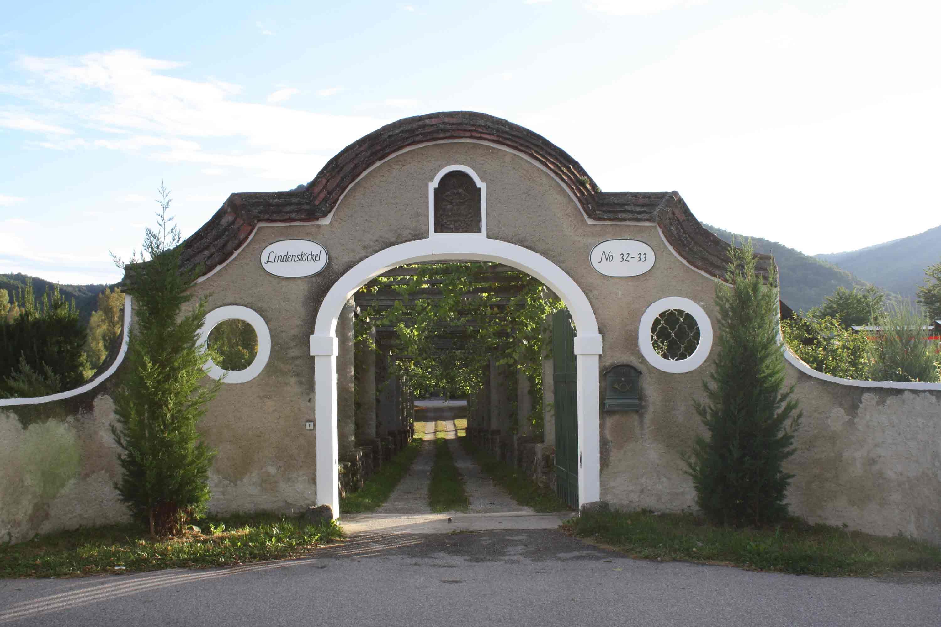 Entrance gate with round arch and inscription 'Lindenstöckel', surrounded by nature.