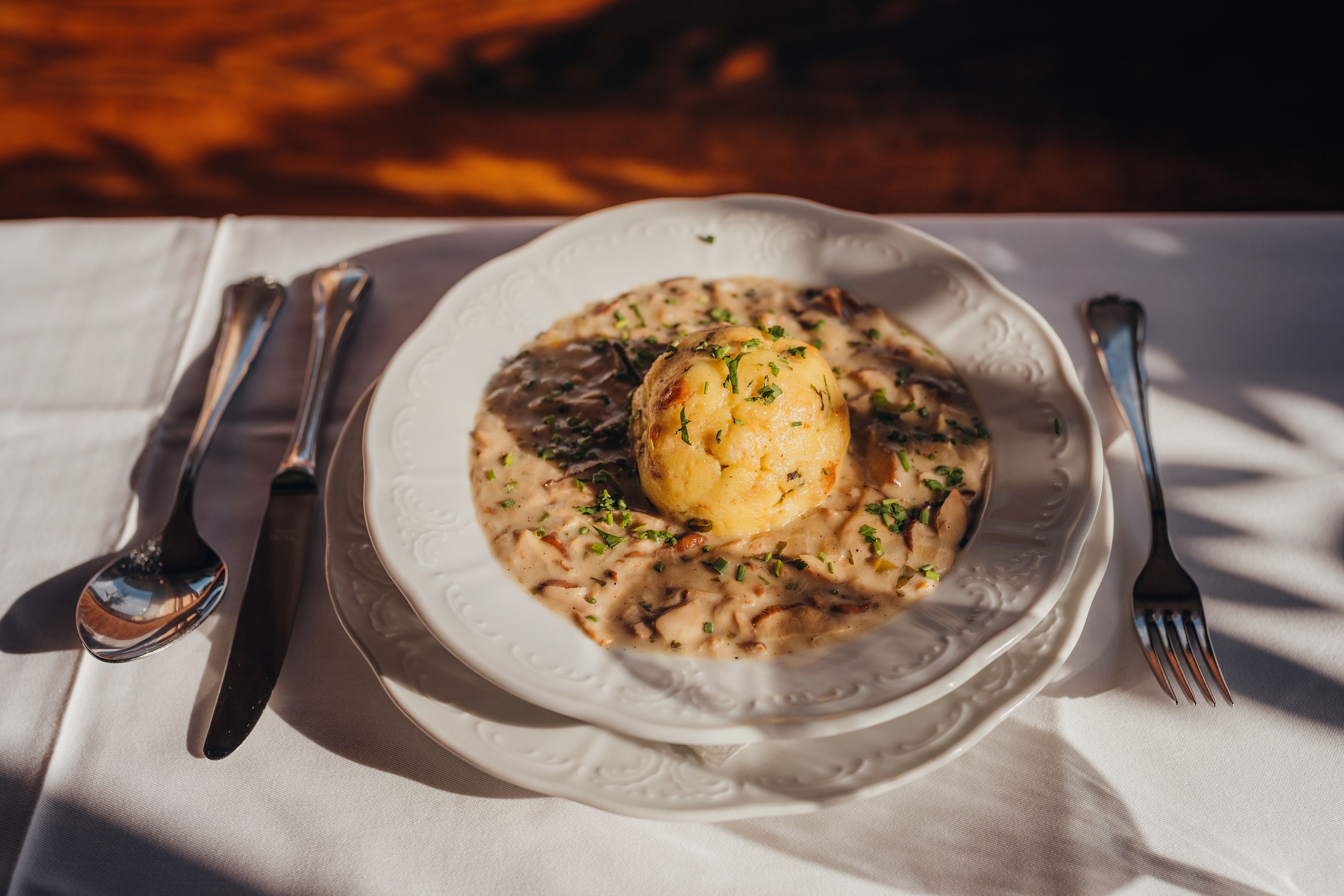A plate with mushroom sauce and a semolina dumpling, garnished with parsley, on a white tablecloth.