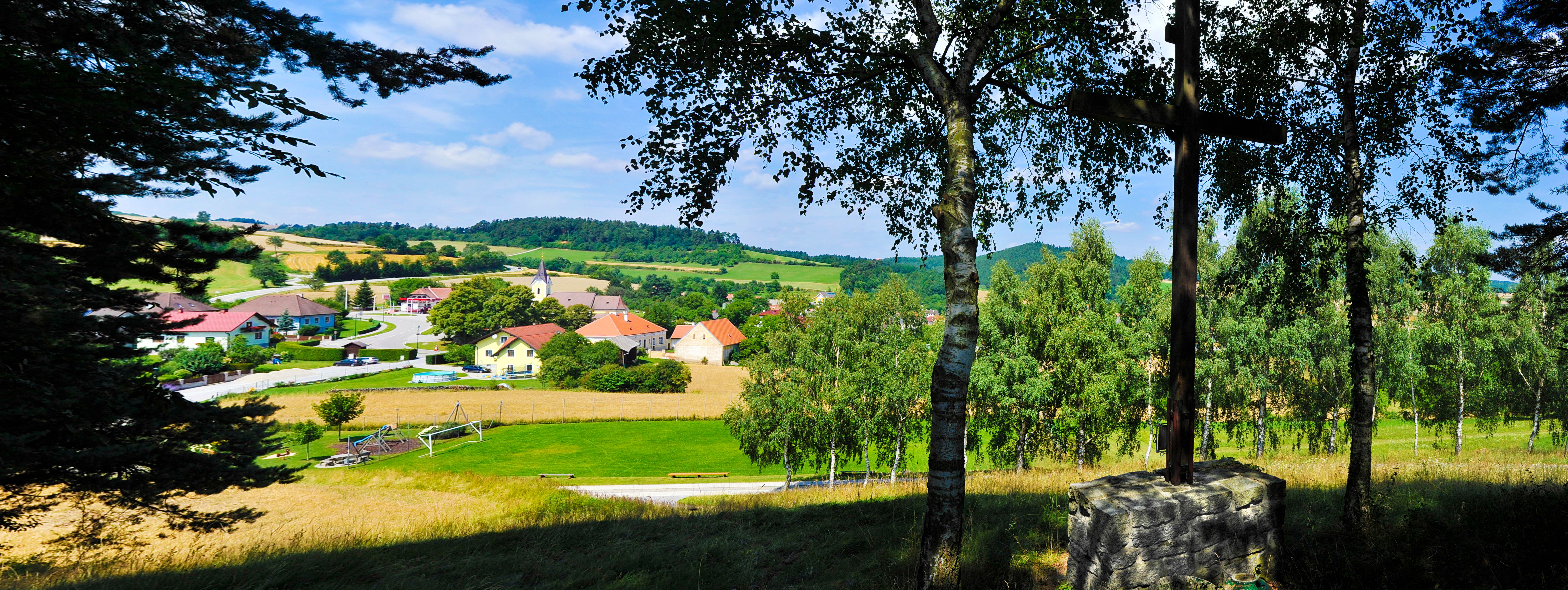 View of a rural community with a church and houses, surrounded by fields and trees.