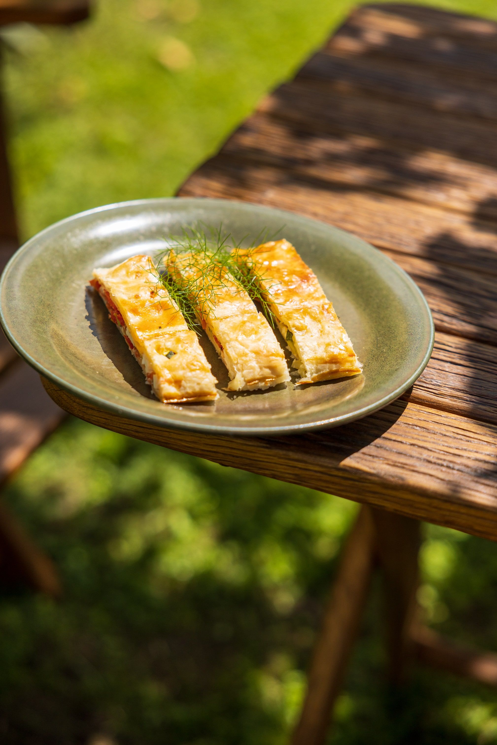 Three pieces of vegetable strudel on a green plate outside.