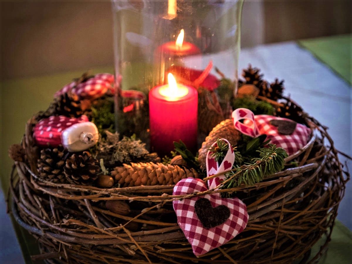 An Advent wreath with a burning red candle, pine cones and red and white checkered fabric hearts.