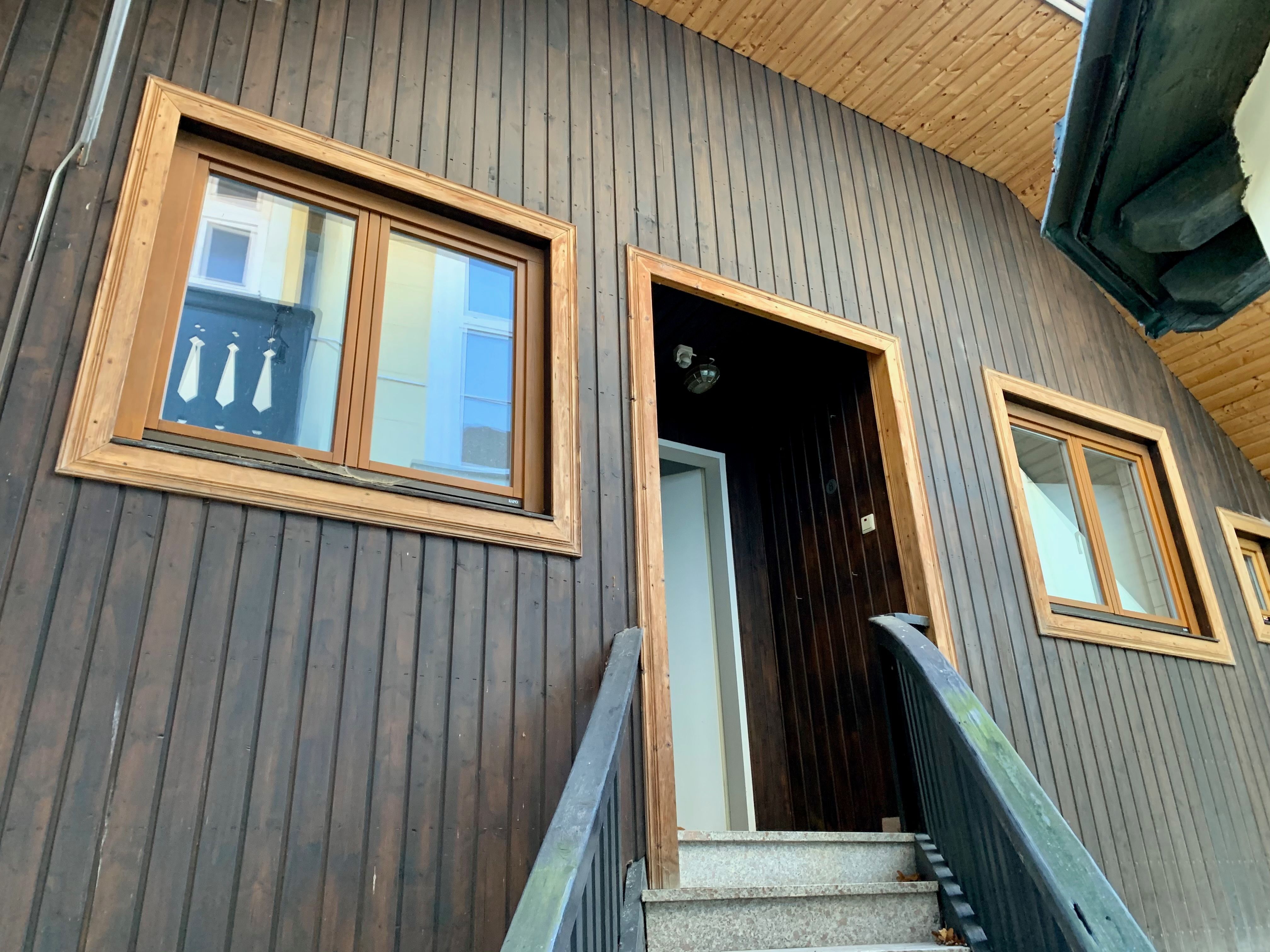 Close-up of a house facade with wooden wall and windows.