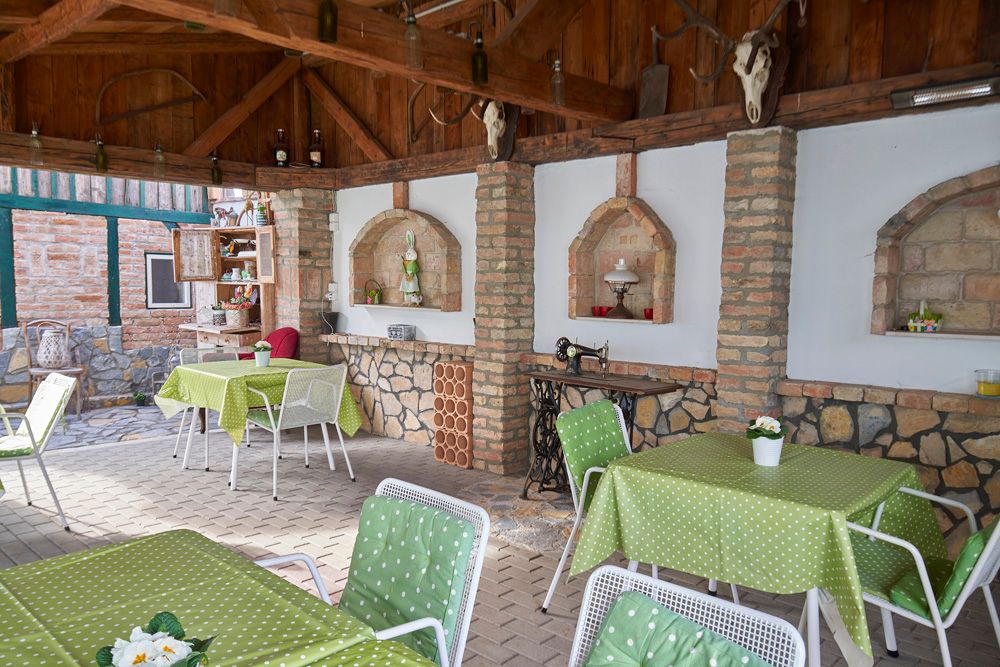 Covered terrace with green tablecloths, white chairs and rustic decorations.