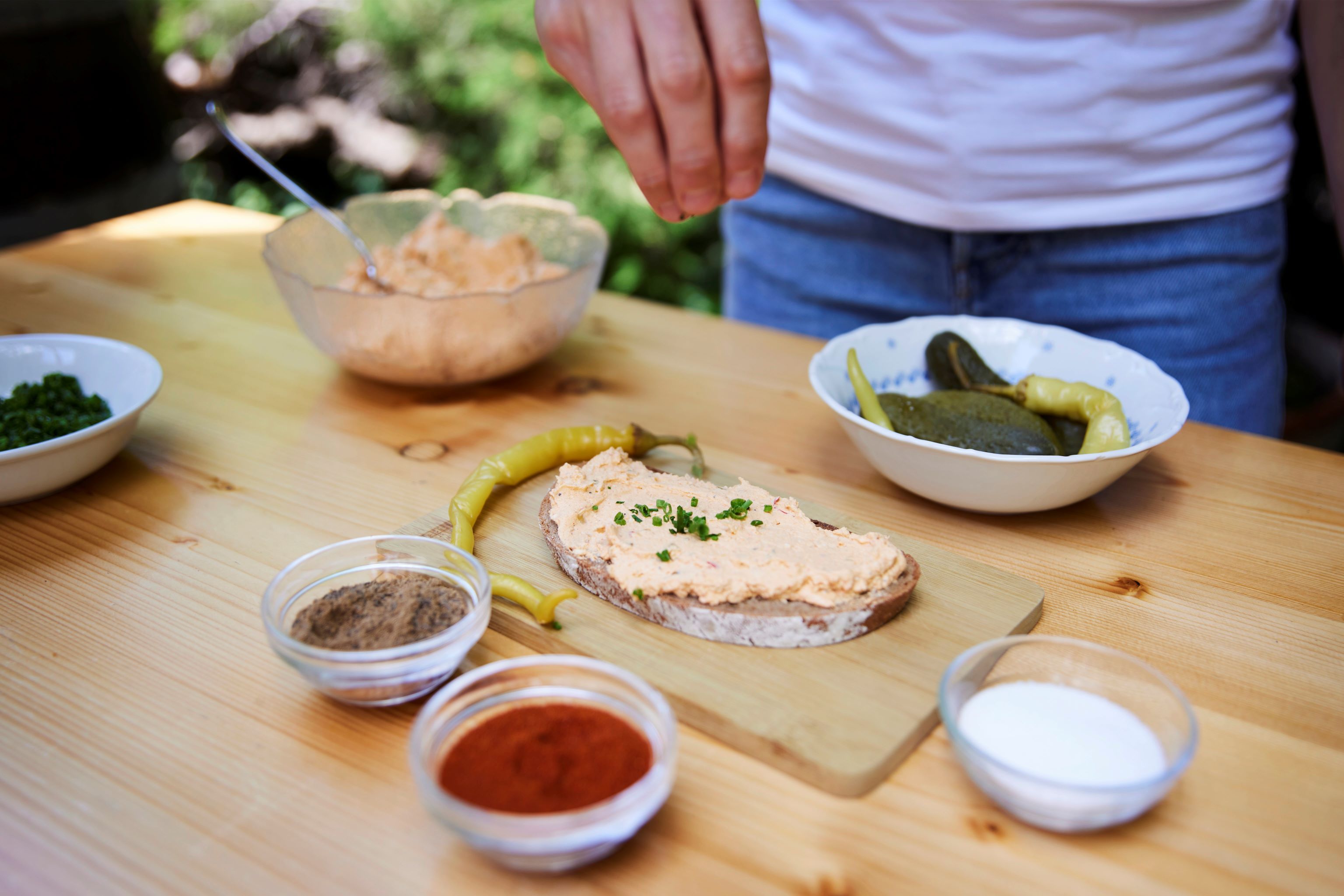 Liptauer bread on a wooden board, surrounded by spices and pickled vegetables.