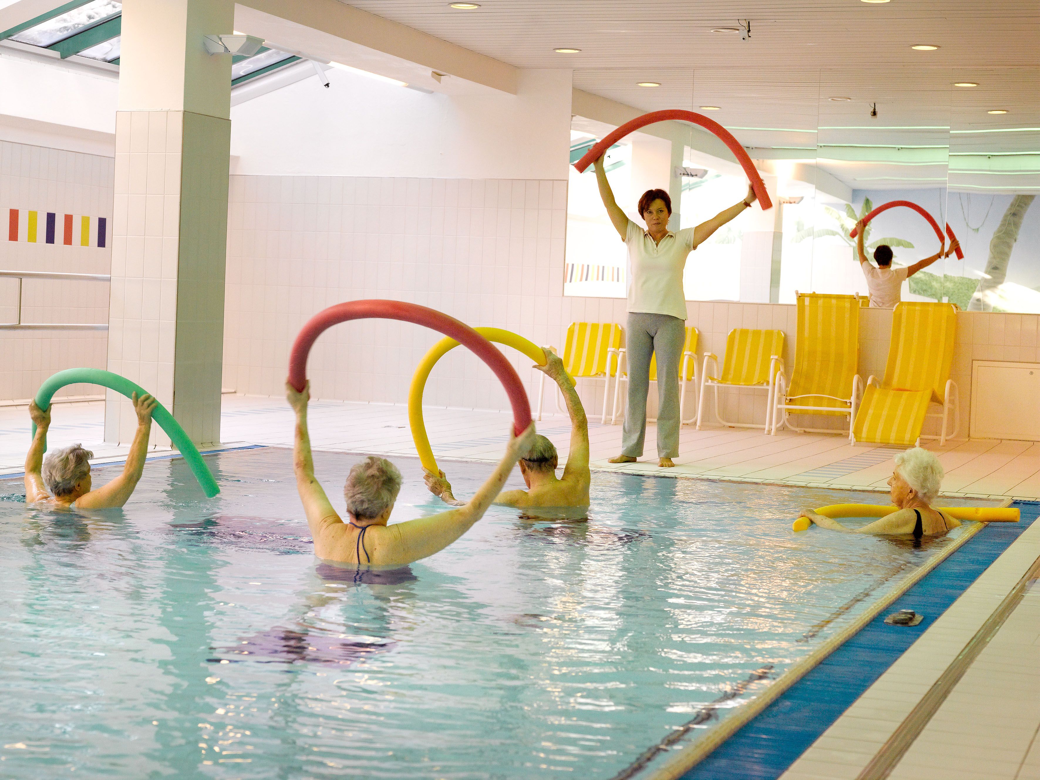 Senior citizens group doing water aerobics in the indoor pool with swimming noodles.