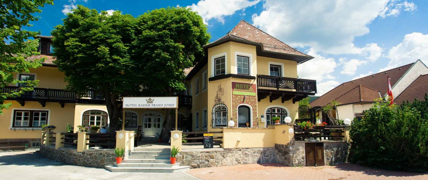 Entrance to the Hotel Kaiser Franz Josef with yellow façade and balcony.