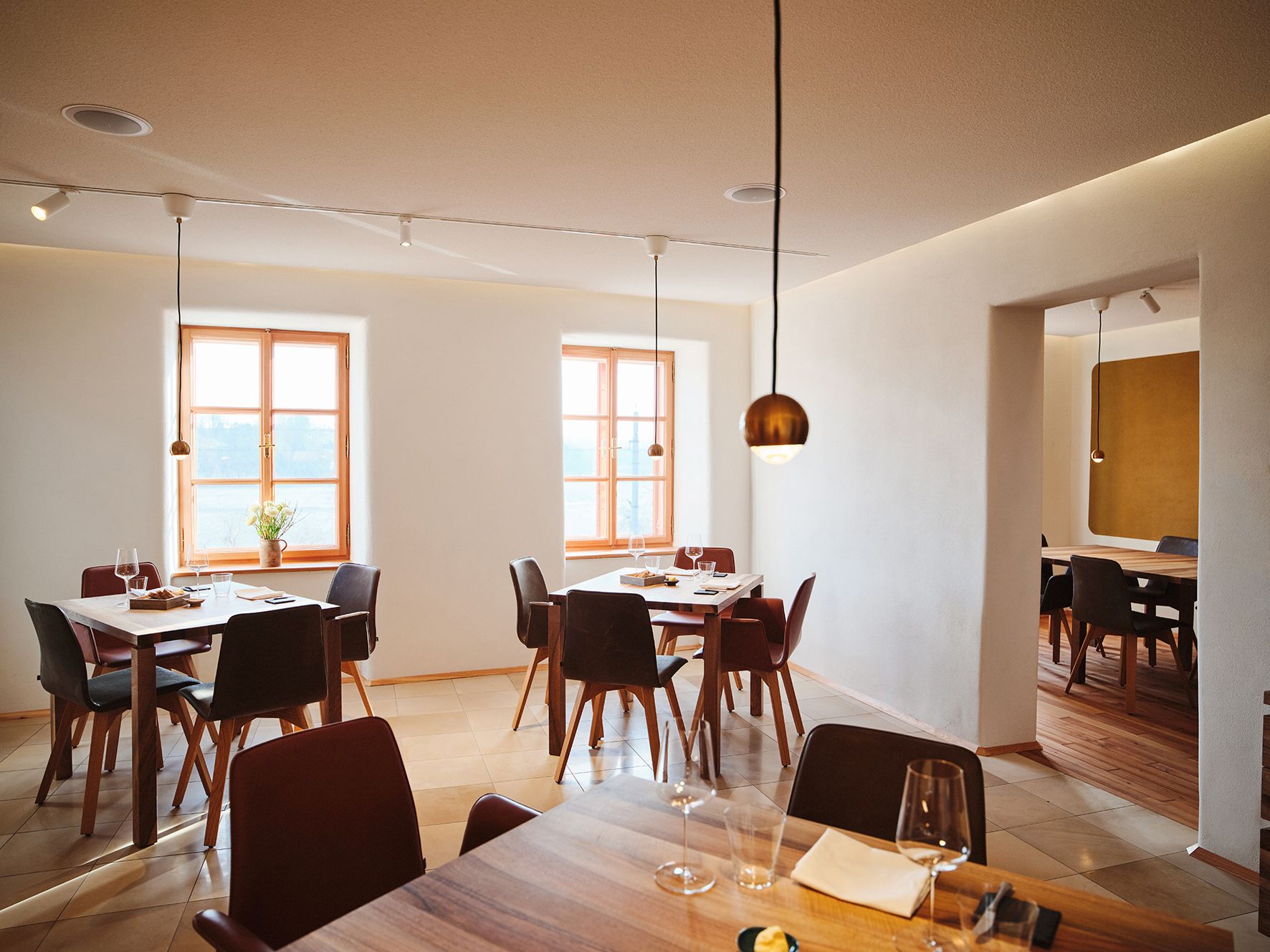 Modern dining room with wooden tables, wine glasses and large windows in a minimalist design.