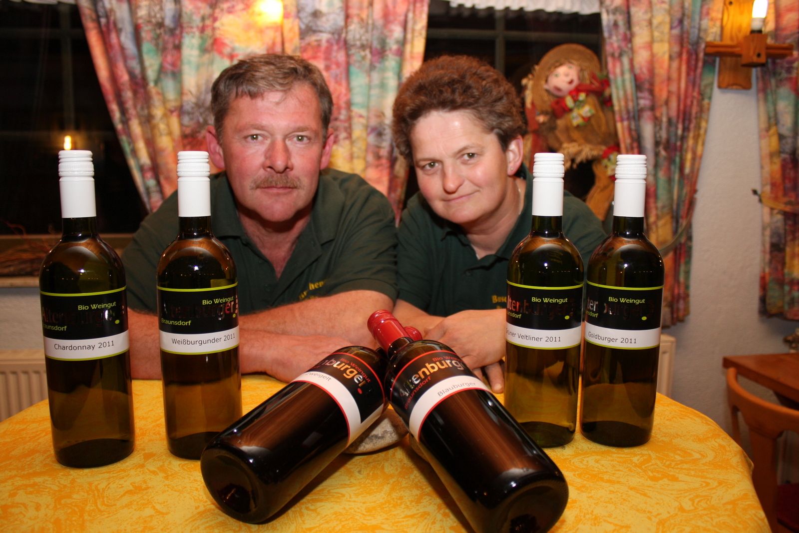 Two people behind a table with bottles of wine.