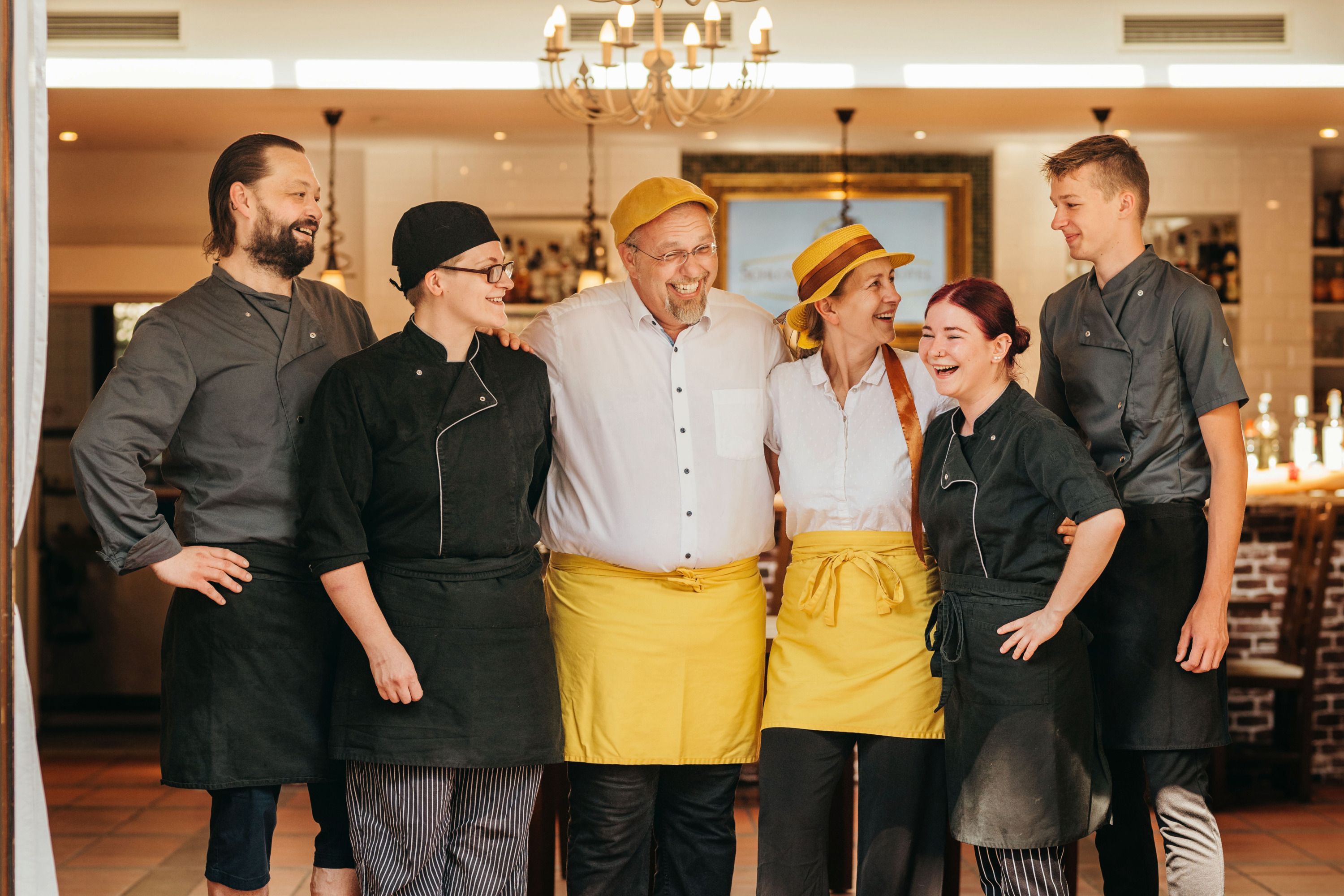 A cheerful team of six people in work clothes stands smiling in a restaurant.