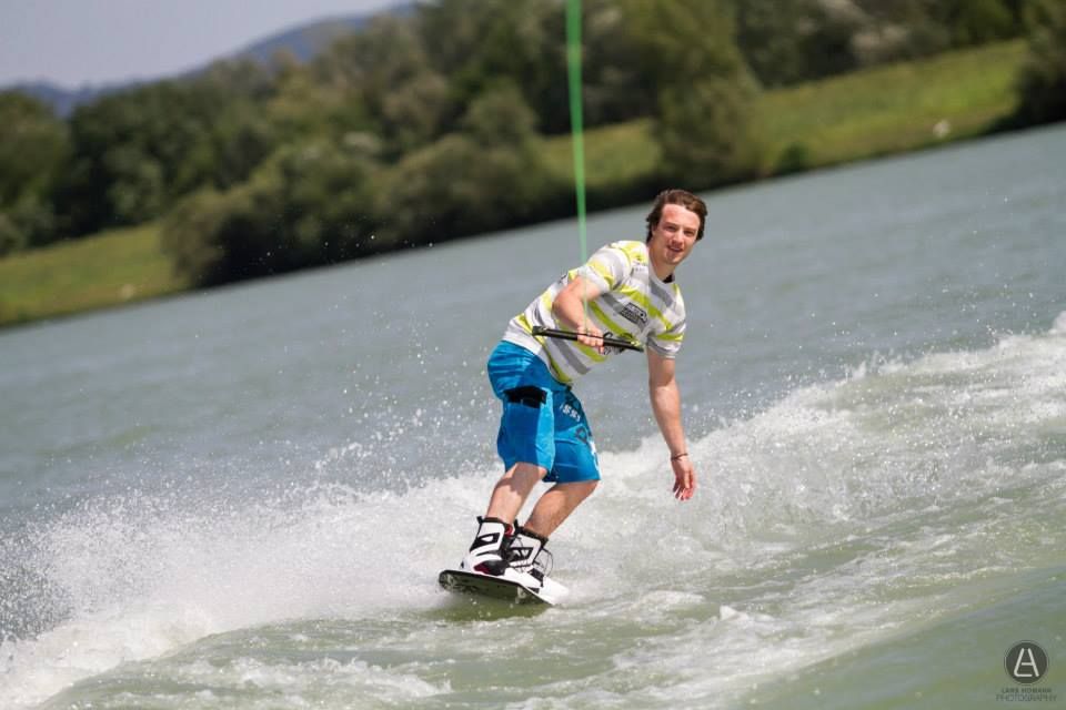 A wakeboarder rides on a lake surrounded by a green landscape.