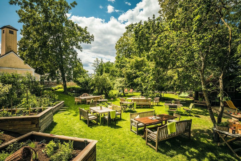 Garden with lush greenery and wooden furniture at tables, blue sky 