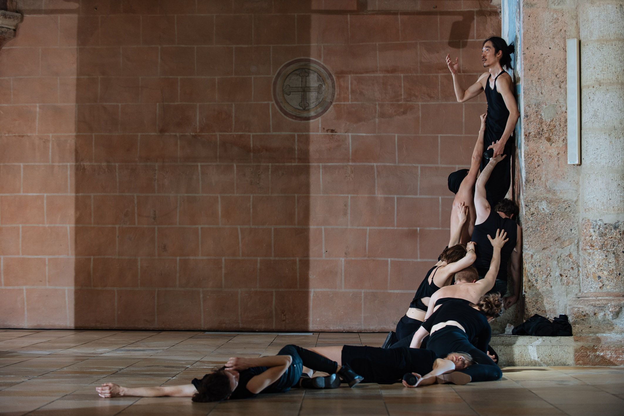 In einem eindrucksvollen Raum entfaltet sich eine dynamische Choreografie, in der die Tänzer in einem kraftvollen Zusammenspiel von Bewegung und Emotionen agieren. Die Lichtverhältnisse schaffen eine mystische Atmosphäre, die die Zuschauer in ihren Bann zieht und die Intensität der Darbietung verstärkt.