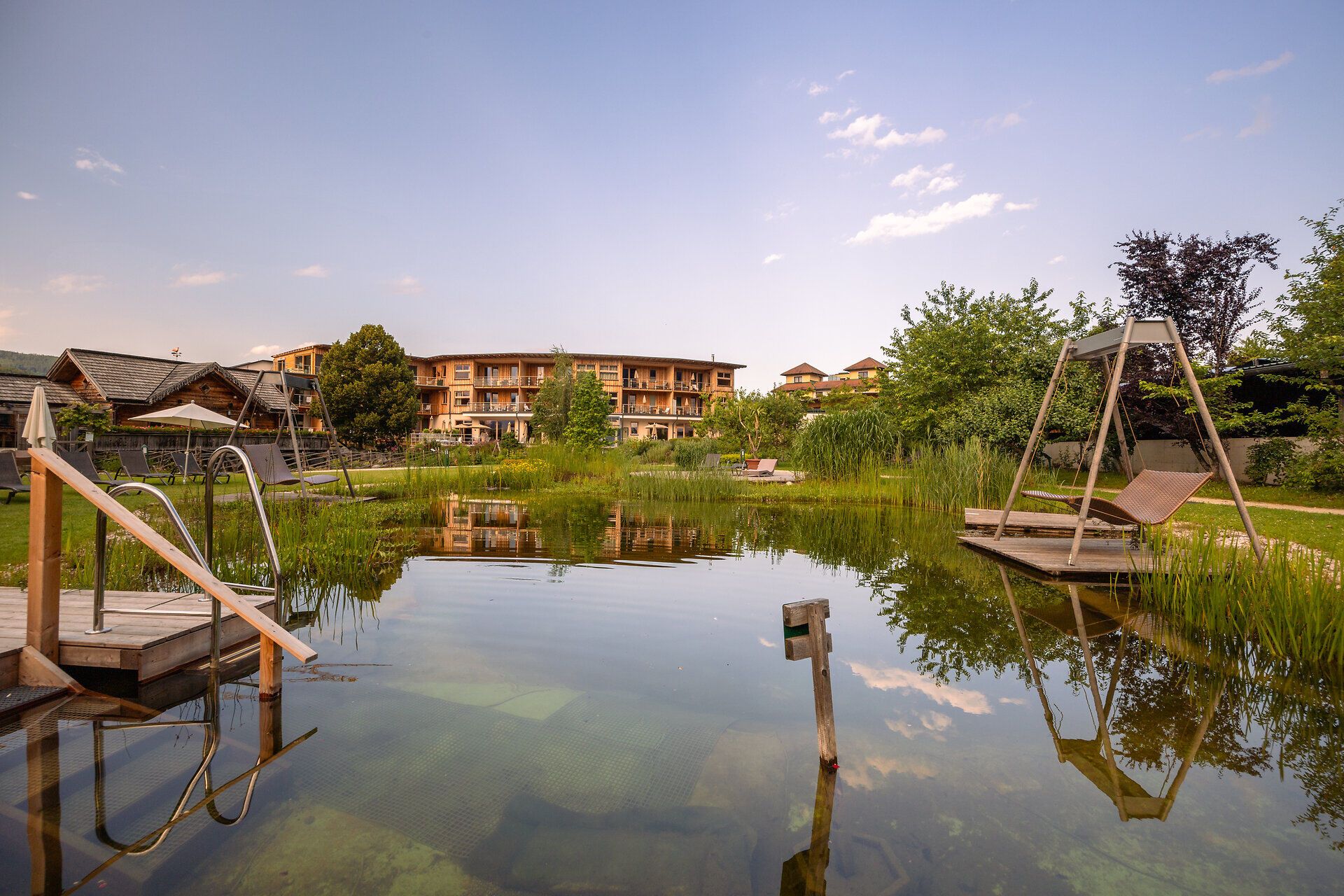 Naturhotel Molzbachhof with pond and deckchairs in the foreground.