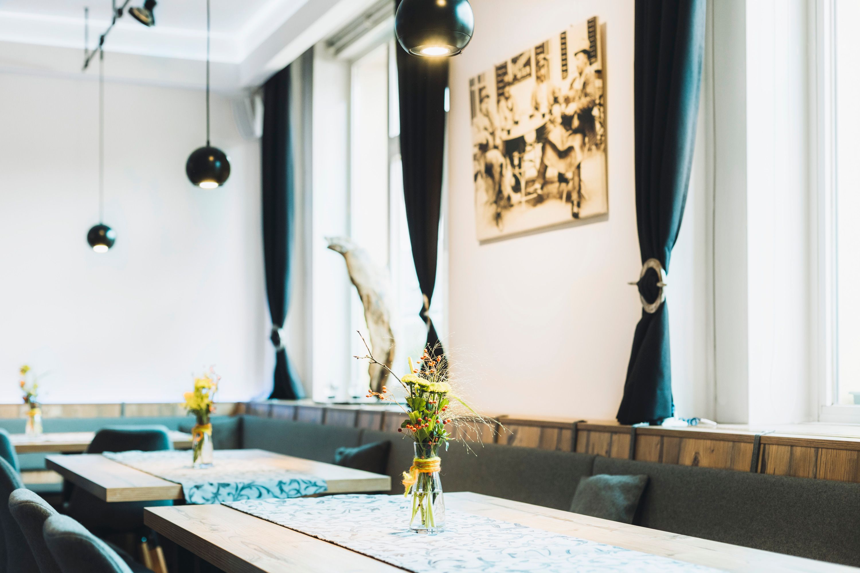 Interior view of a stylish café with wooden tables, flower vases and black curtains.
