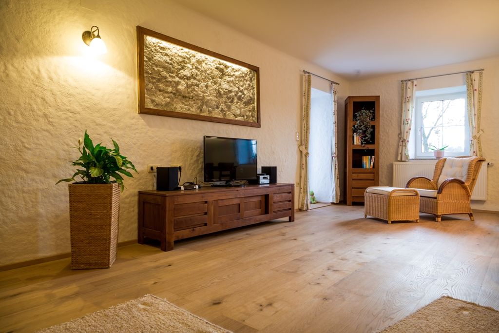 Cozy living room with wooden furniture, TV, rattan armchair and plants.