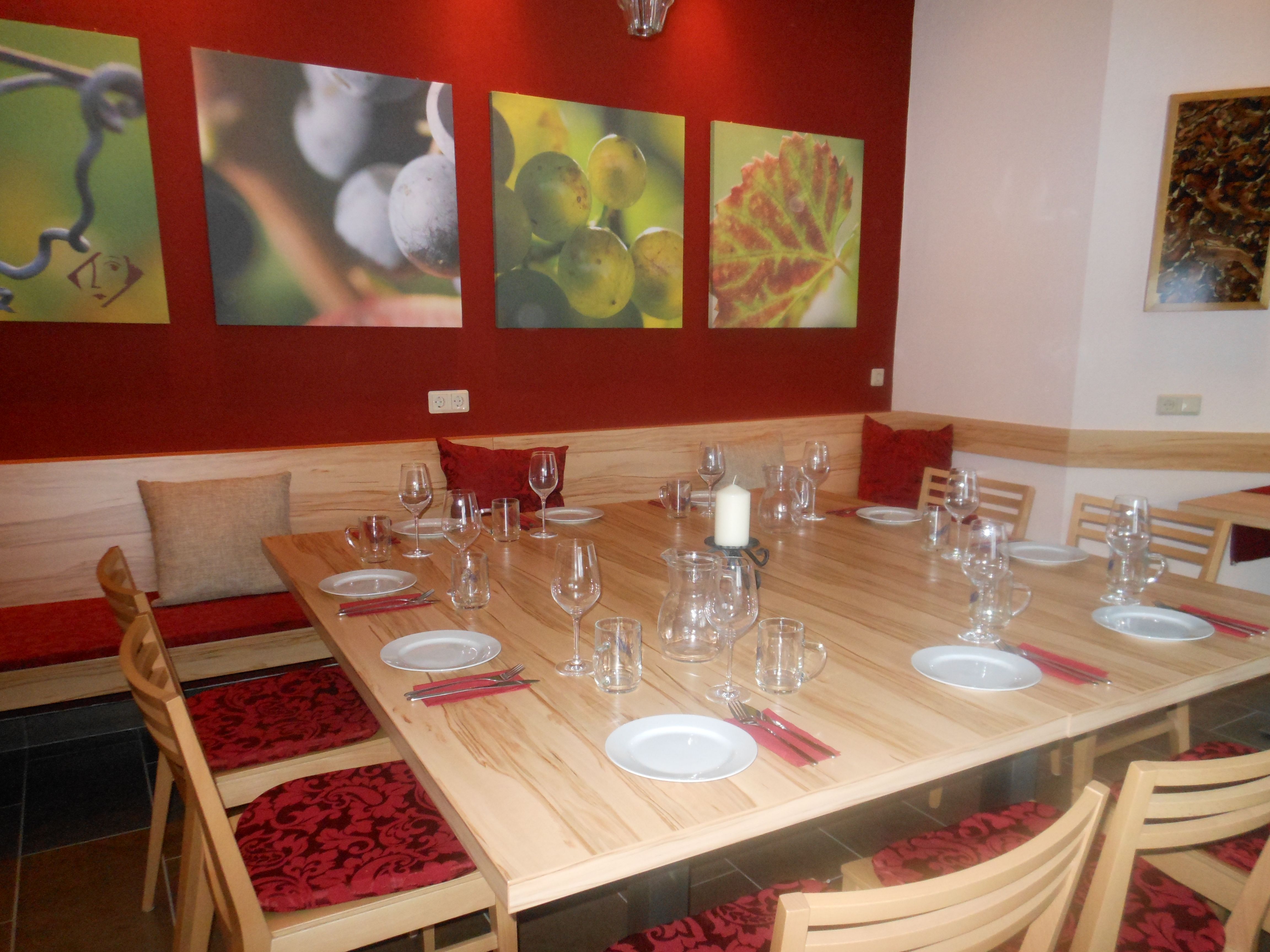 A tasting room with a covered wooden table, wine glasses and murals of grapes.
