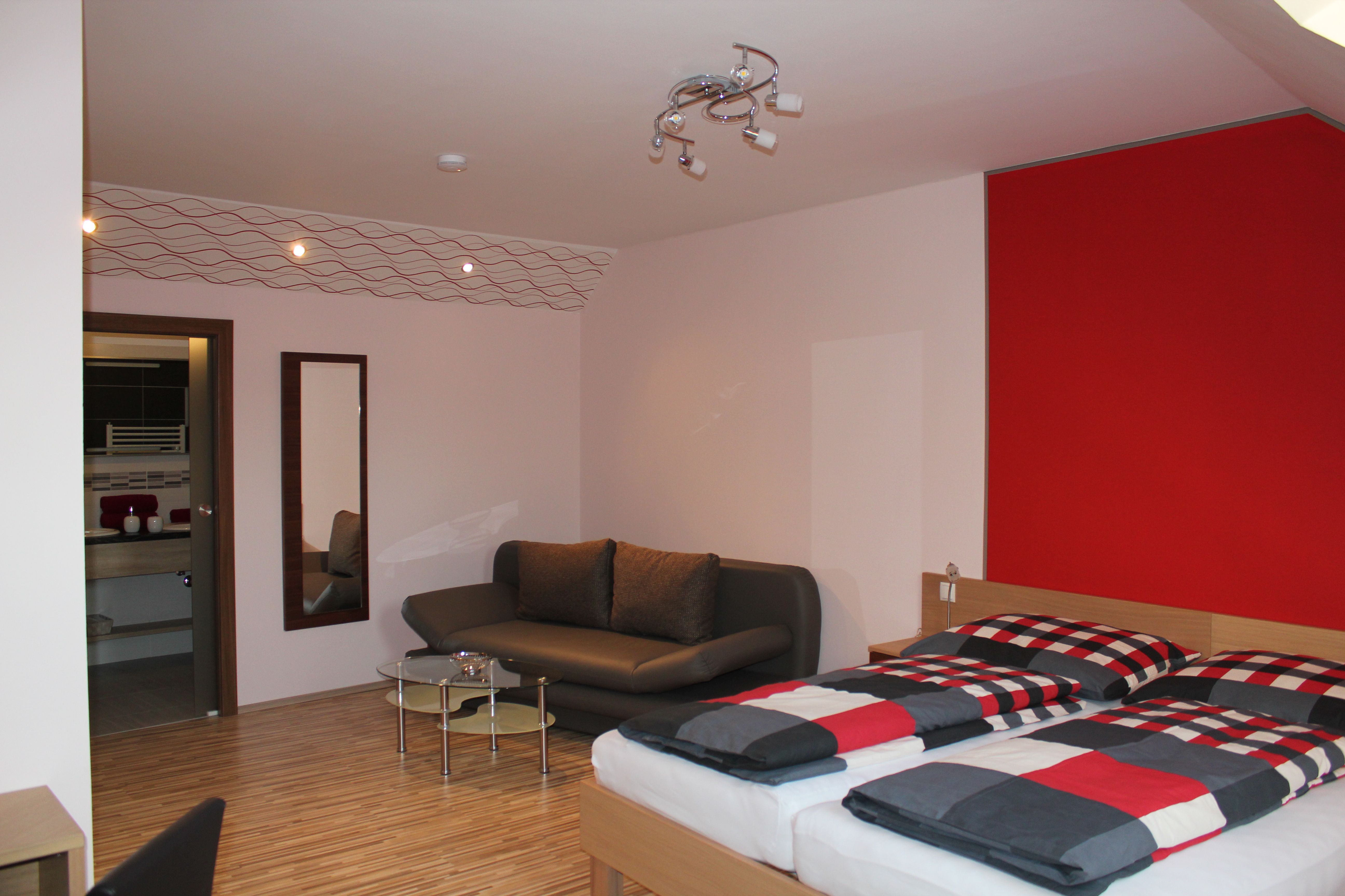 Modern furnished guest room with double bed, sofa and small table.