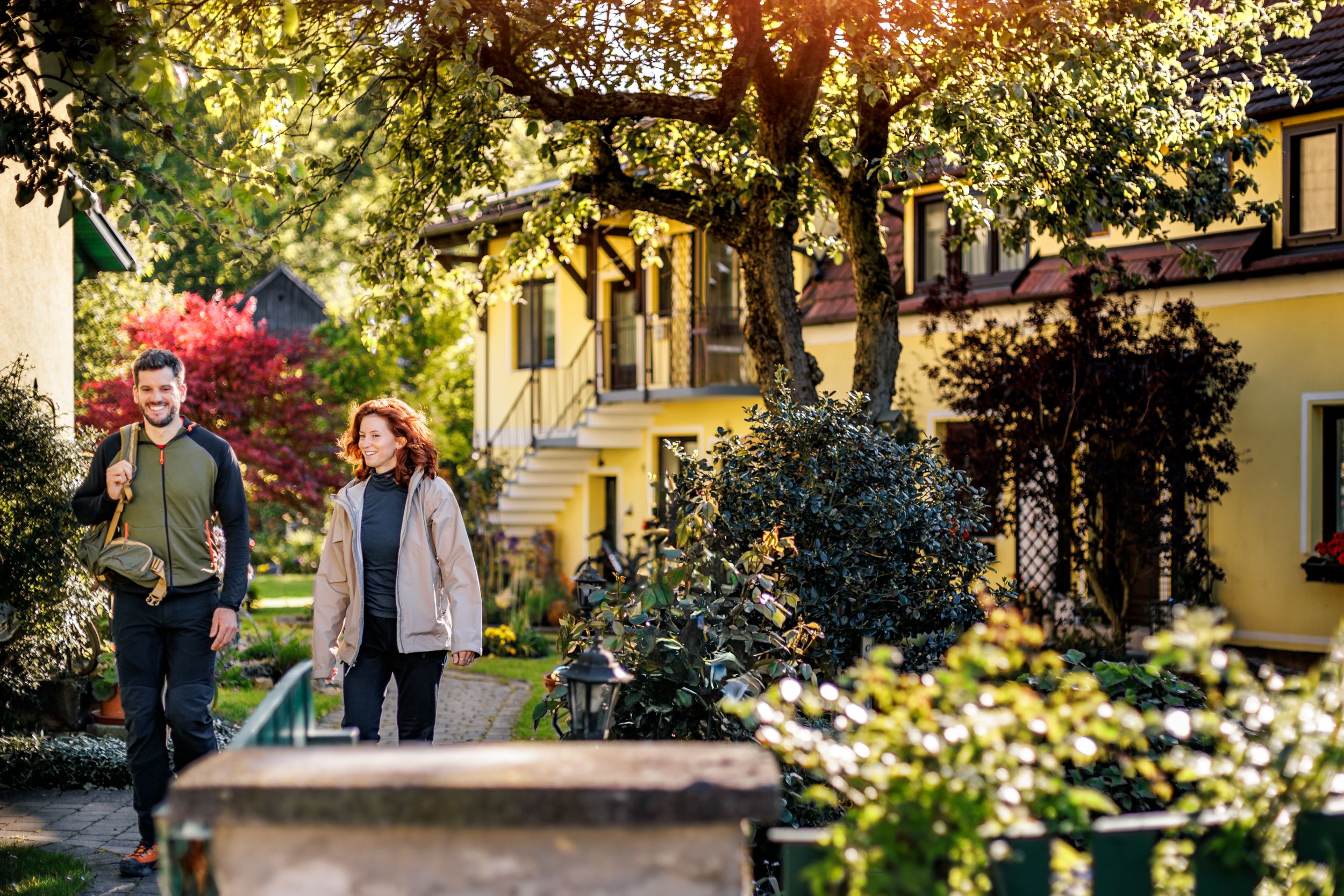 A man and a woman in hiking gear walk through the green, well-tended garden of the Pension Hendling