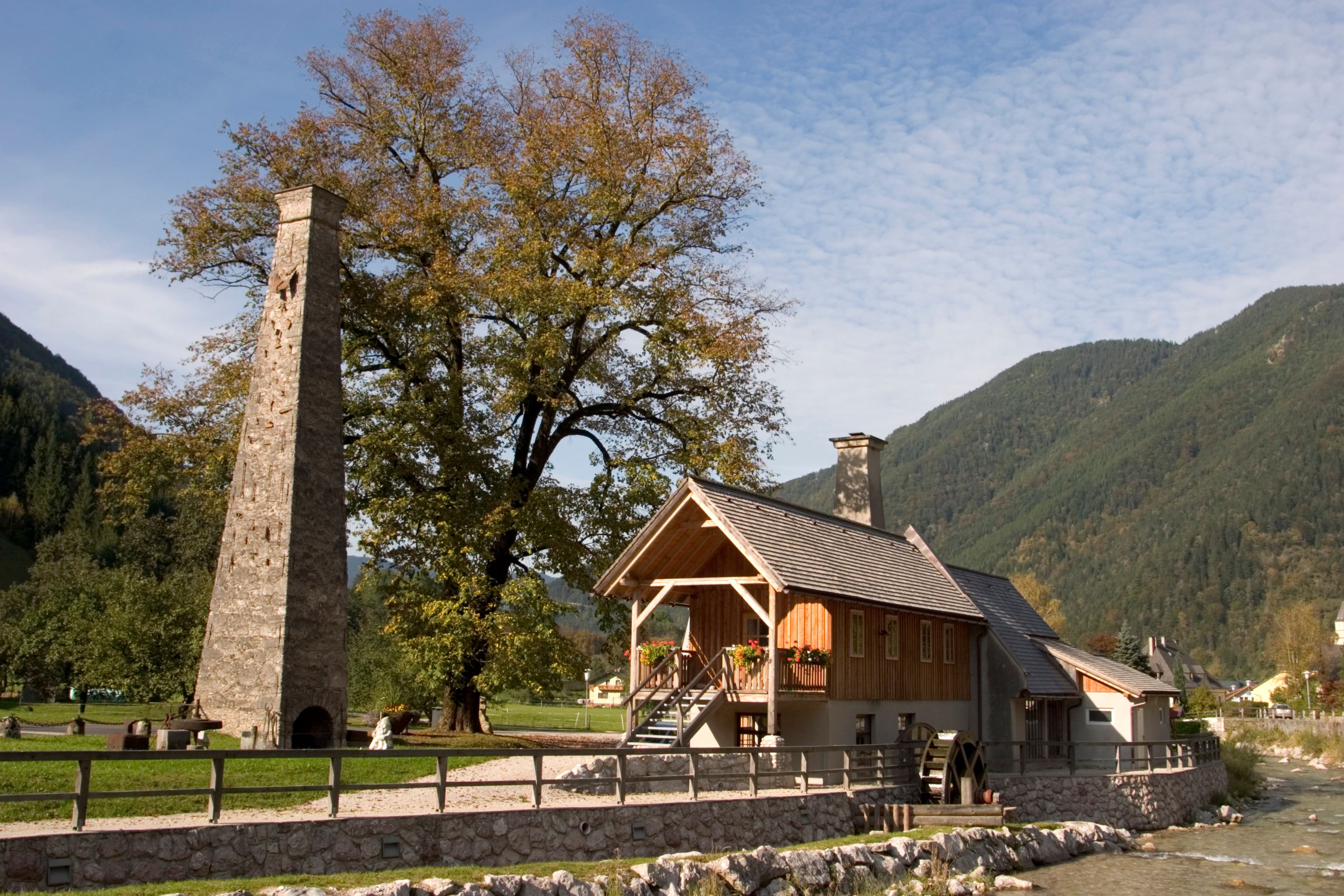 Historic building with chimney and water wheel in a rural setting.