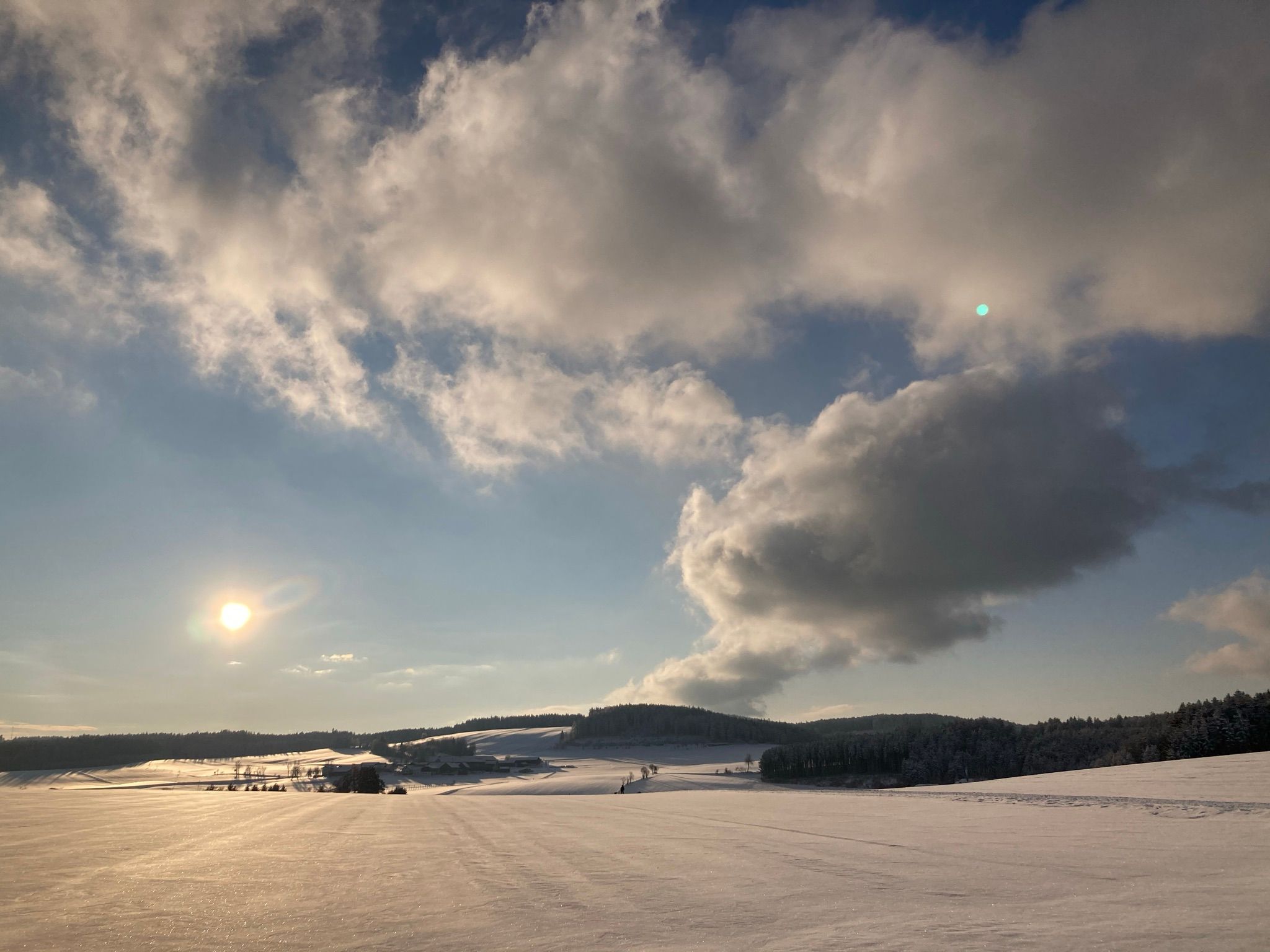 Snow-covered landscape under a cloudy sky with a low sun.