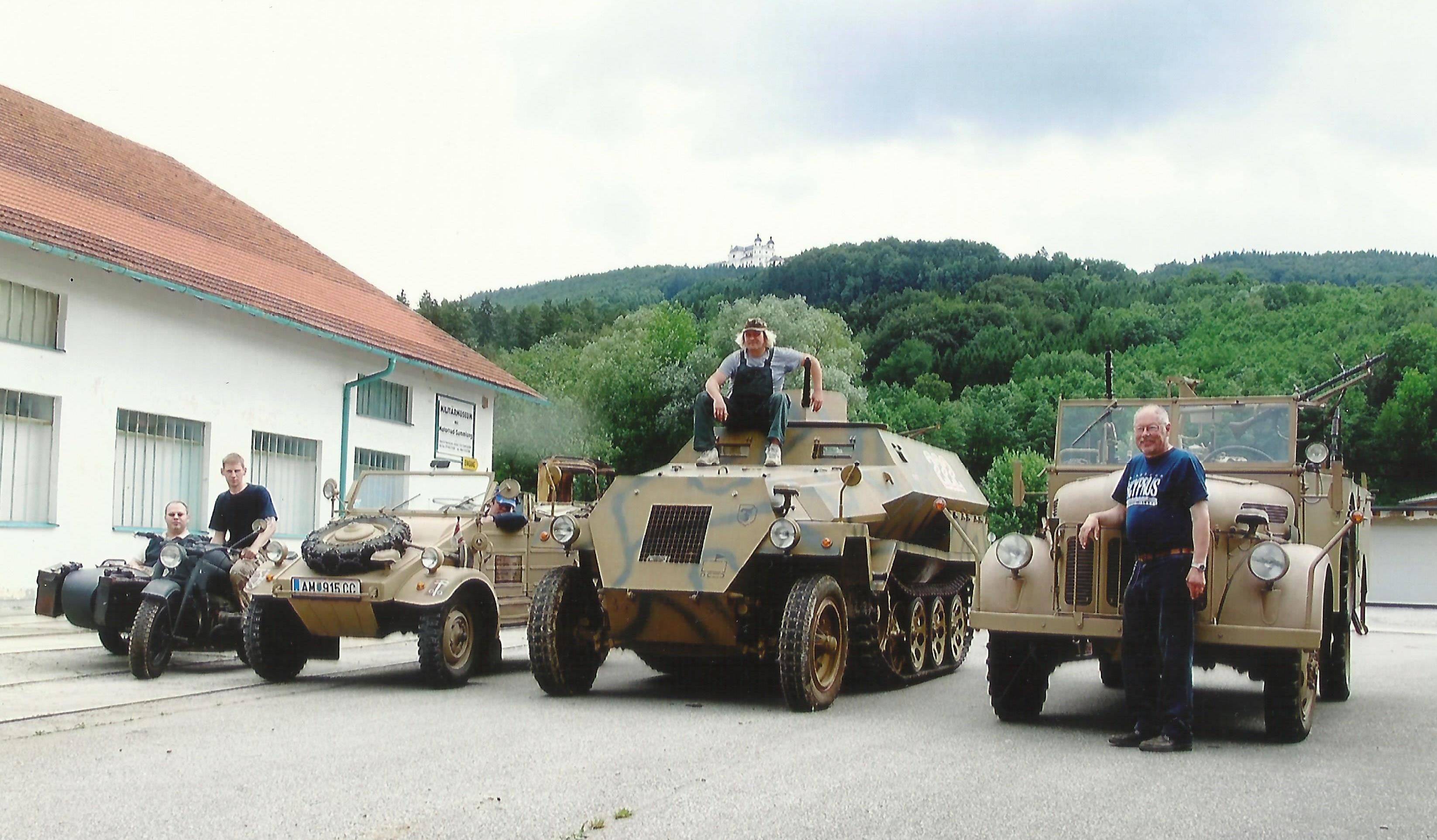 Military vehicles in front of a building with a hill in the background.