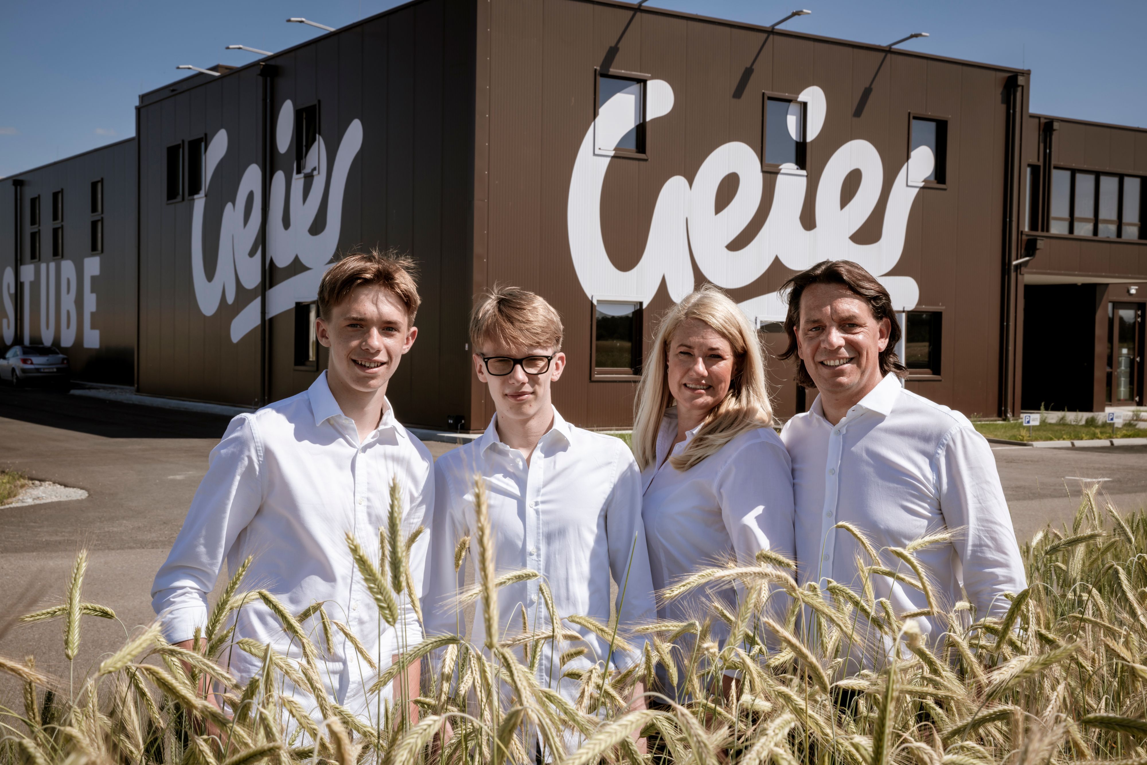 Four people in white clothing are standing in front of a building with the sign 'Geier'.