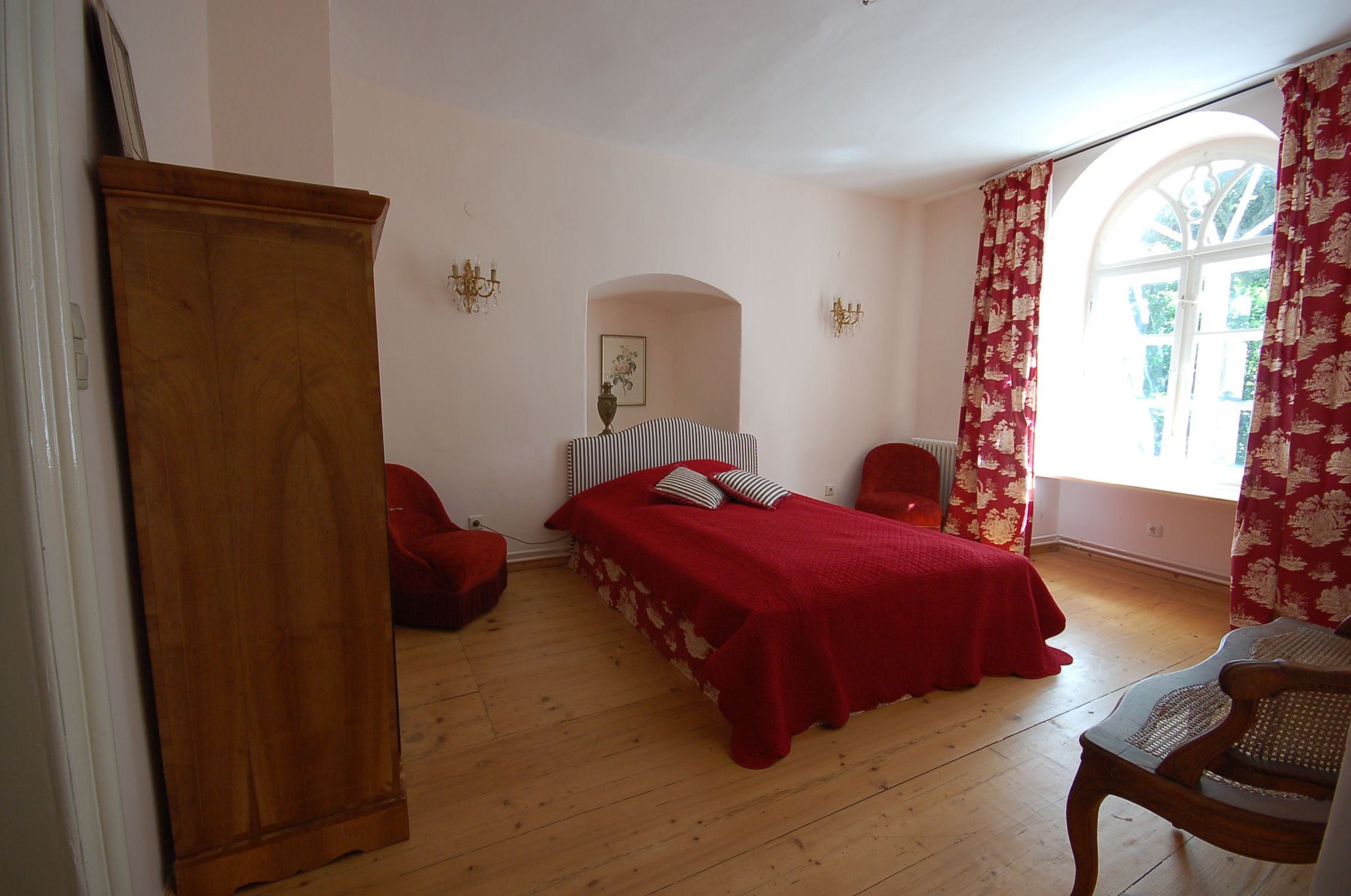 A cozy bedroom with a red bed, red curtains and wooden furniture.
