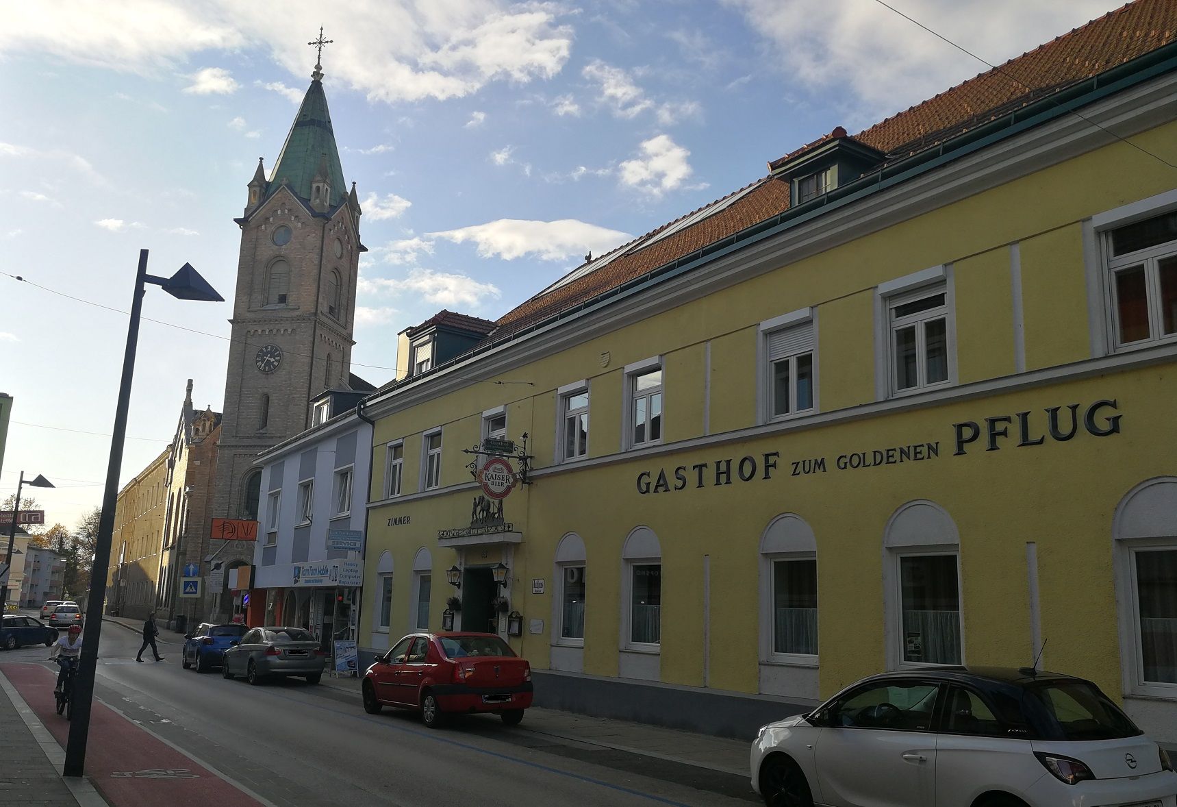 Street scene with yellow building 'Gasthof zum goldenen Pflug' and church tower in the background.