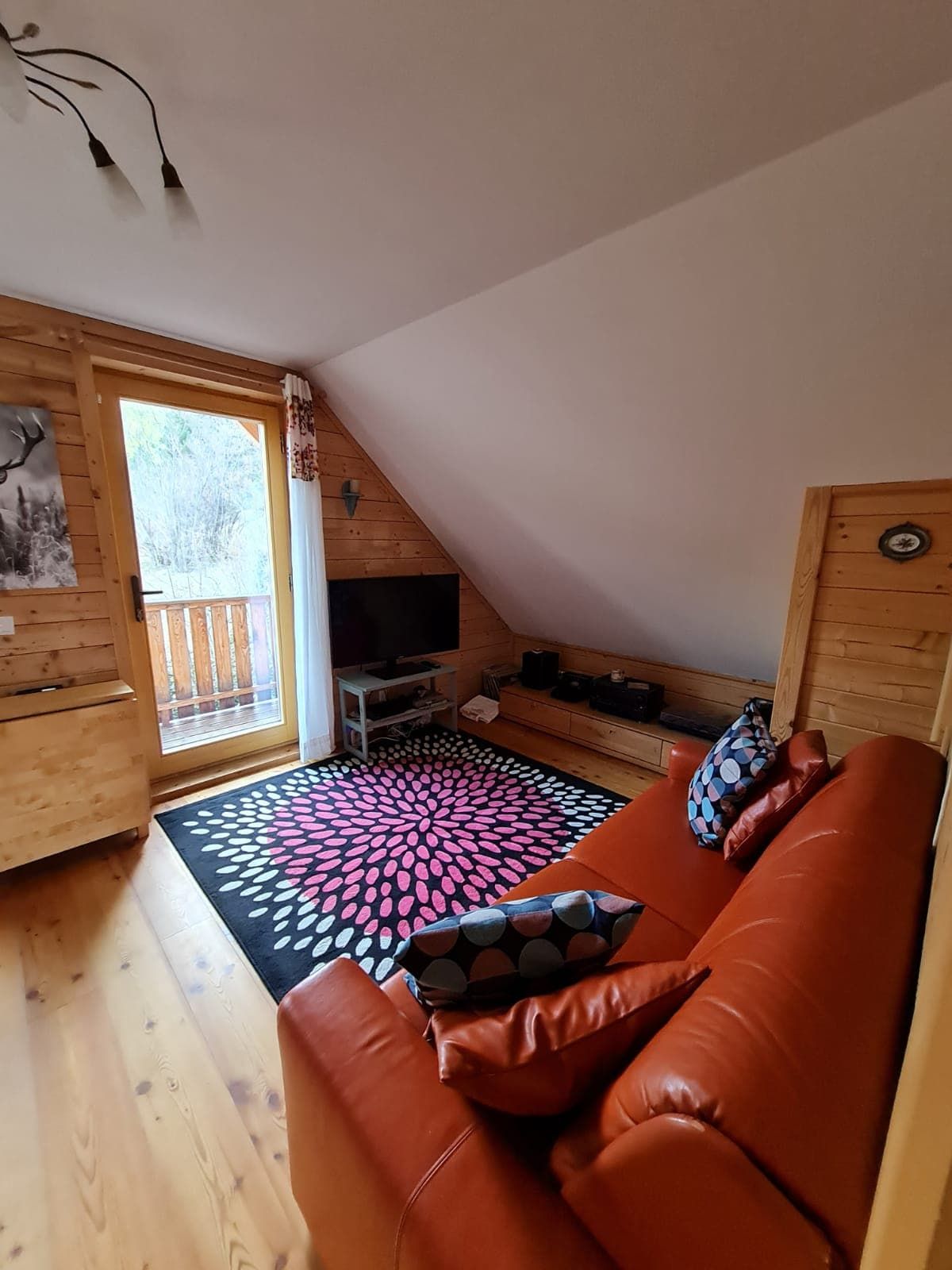 Cozy living room with red sofa, wooden walls and a colorful carpet in front of a balcony window.
