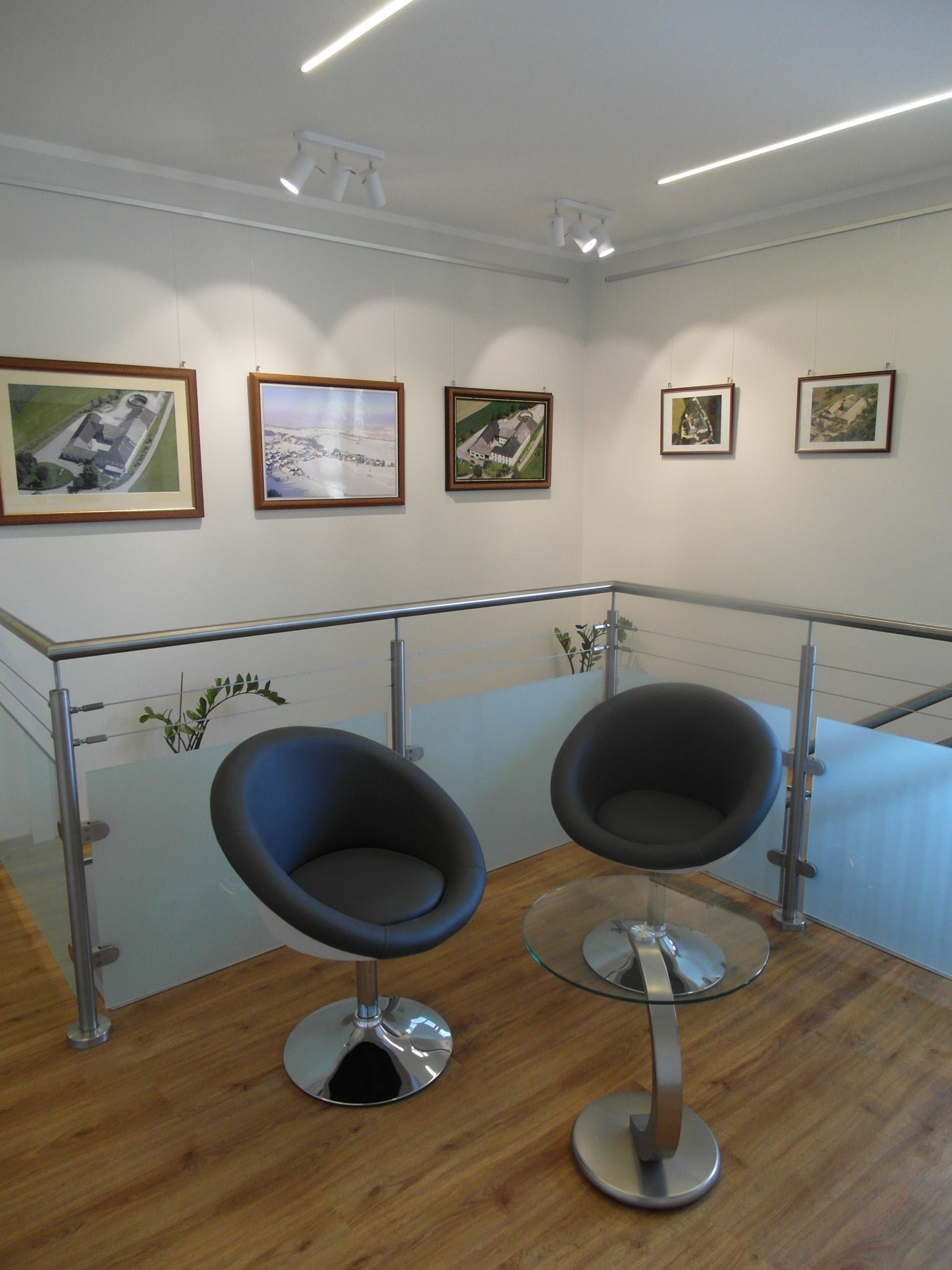 Modern interior with two black chairs and a glass table in front of a wall with framed pictures.